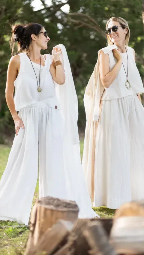 Dos mujeres vestidas de blanco y con gafas de sol, posando al aire libre.