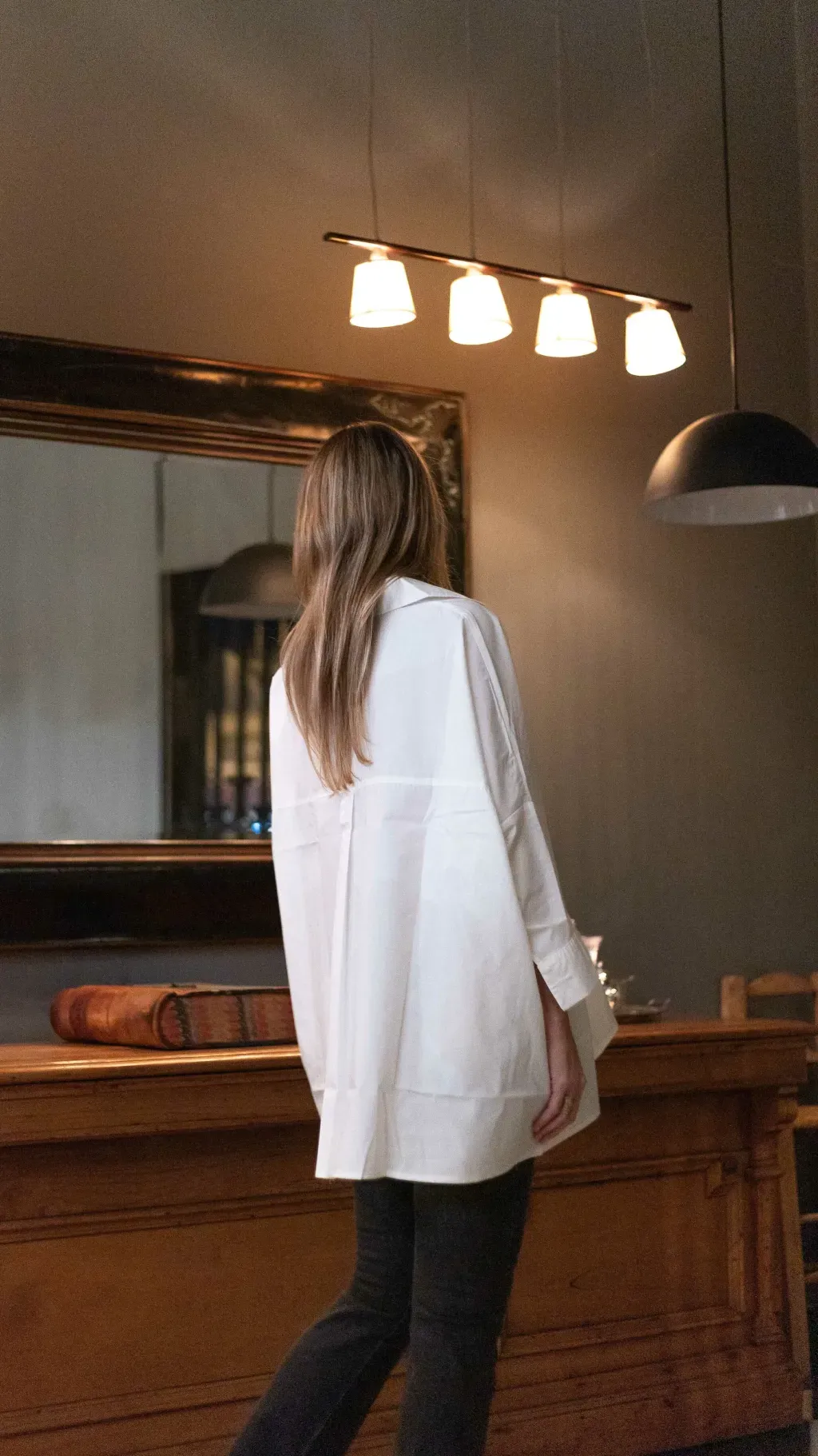 Mujer vestida con una camisa blanca de gran tamaño y pantalones oscuros, con un collar.