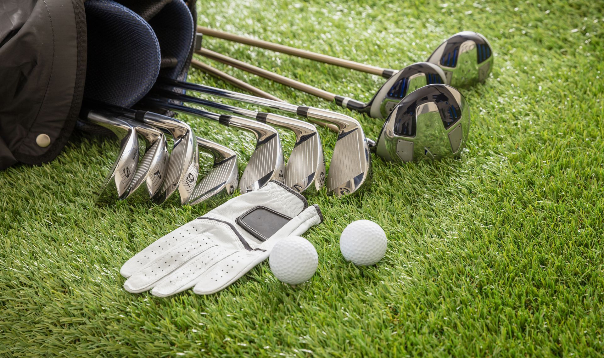 Premium golf equipment with professional clubs, white balls, and a leather glove on the grass.