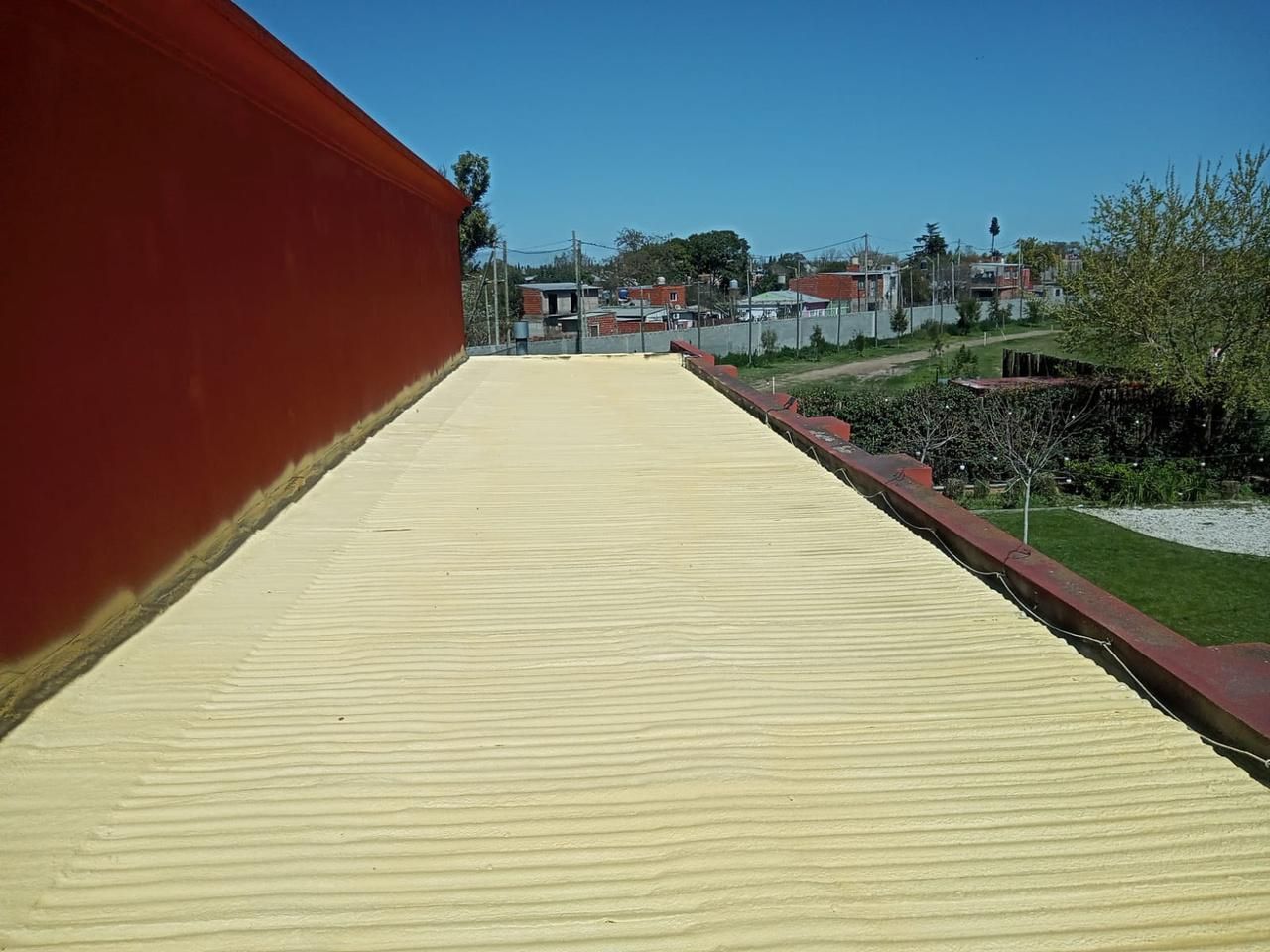 Una azotea con una superficie texturizada de color amarillo, al lado de una pared roja, con una zona residencial al fondo.