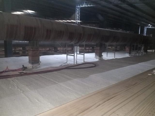 Dentro de un gran edificio industrial, una gran tubería cilíndrica discurre por encima. Una tela blanca cubre el suelo.