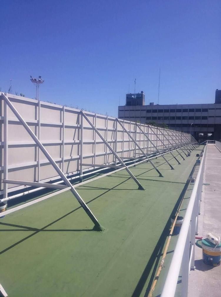 Barrera de metal blanco sobre una superficie verde con un edificio al fondo bajo un cielo azul.