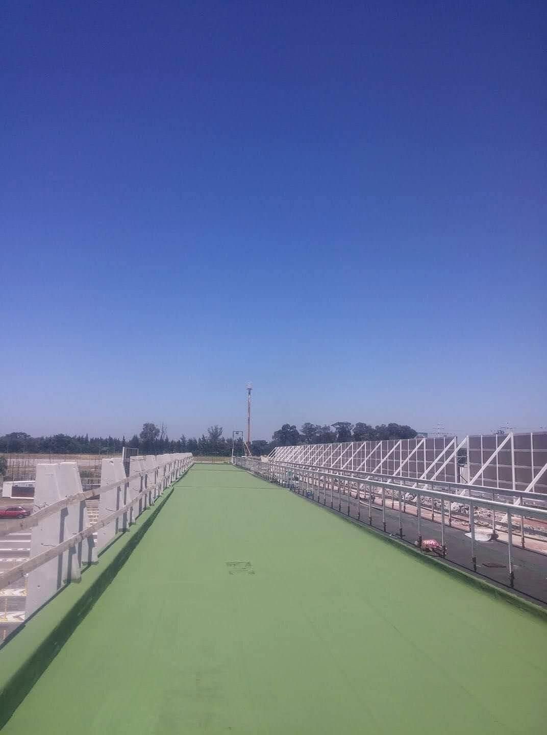 Camino verde con estructuras metálicas, cielo azul, entorno industrial.