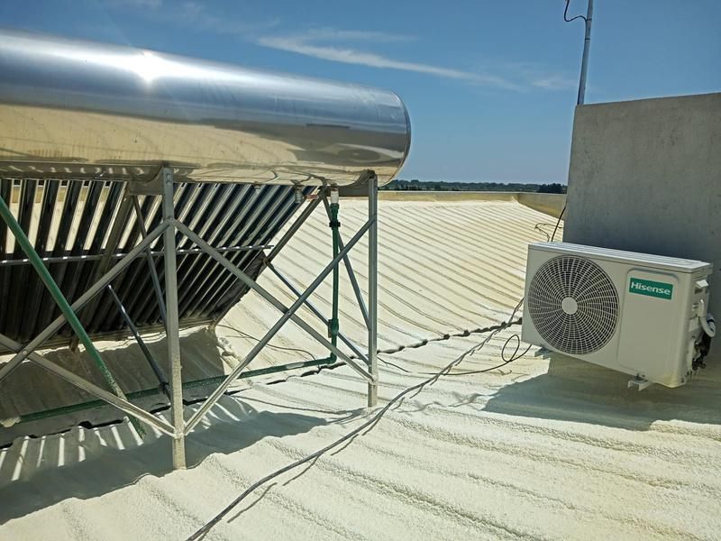 Calentador de agua solar y aire acondicionado sobre un tejado revestido de blanco bajo un cielo azul.