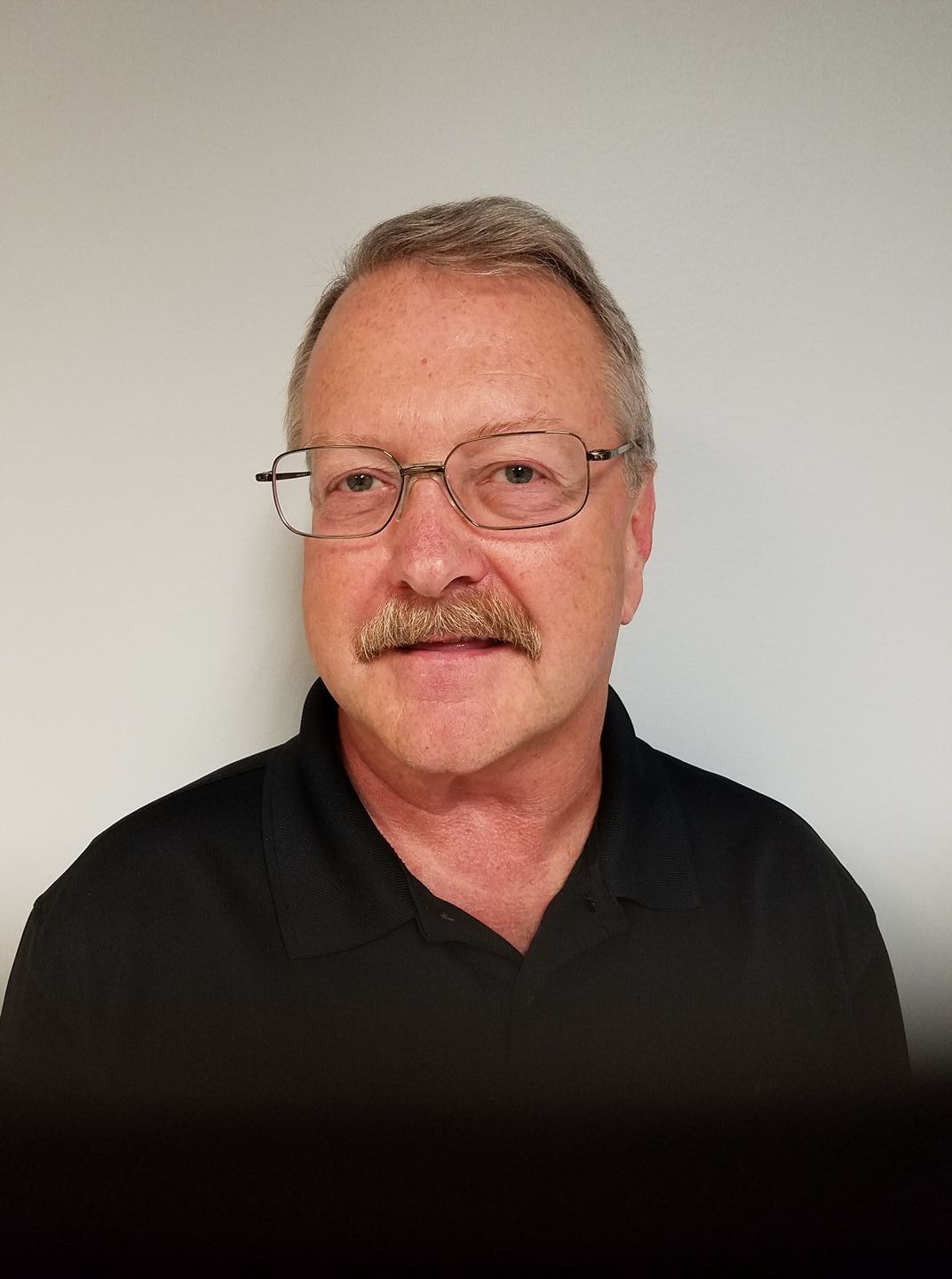 Portrait of a man with glasses and a mustache, wearing a black shirt against a plain light background