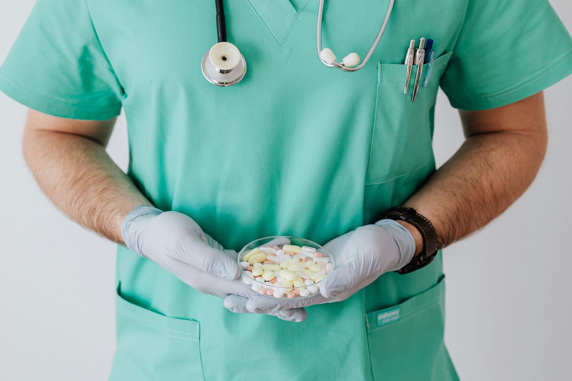 Gloved medical worker in green scrubs holding a cup of pills and capsules