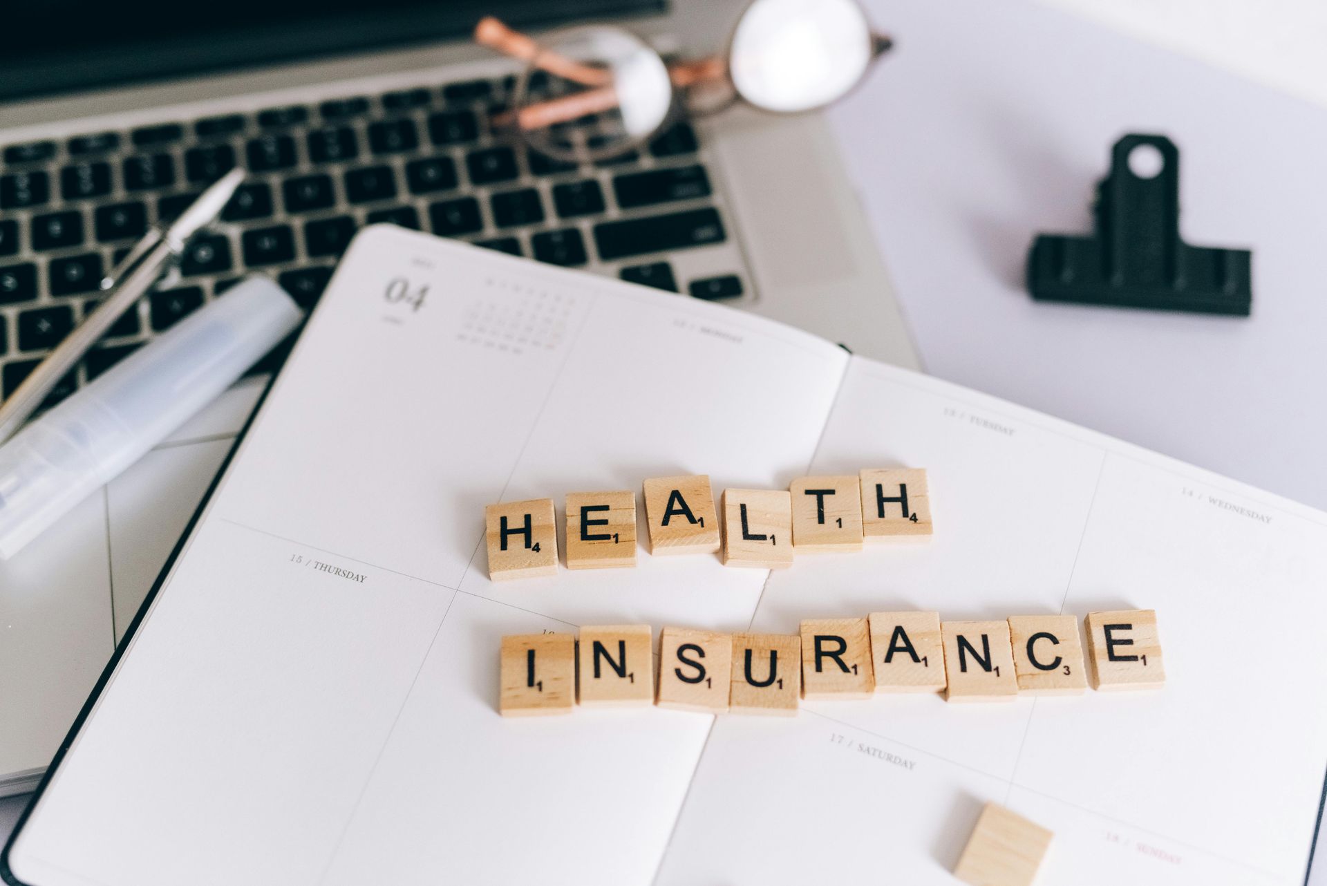Health insurance text spelled with letter tiles on a notebook beside a laptop and office supplies