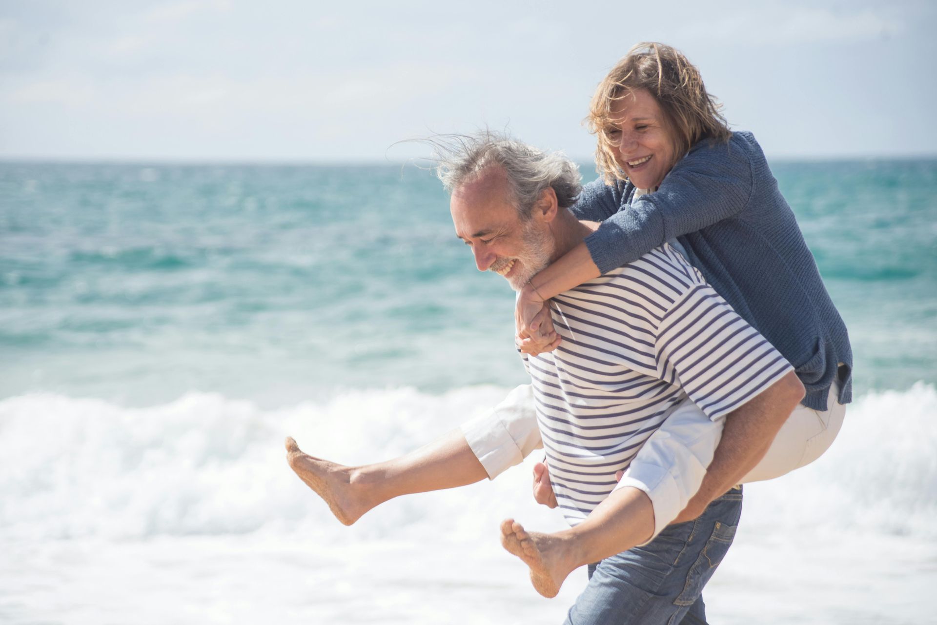 Person giving a piggyback ride on a sunny beach with ocean waves behind them