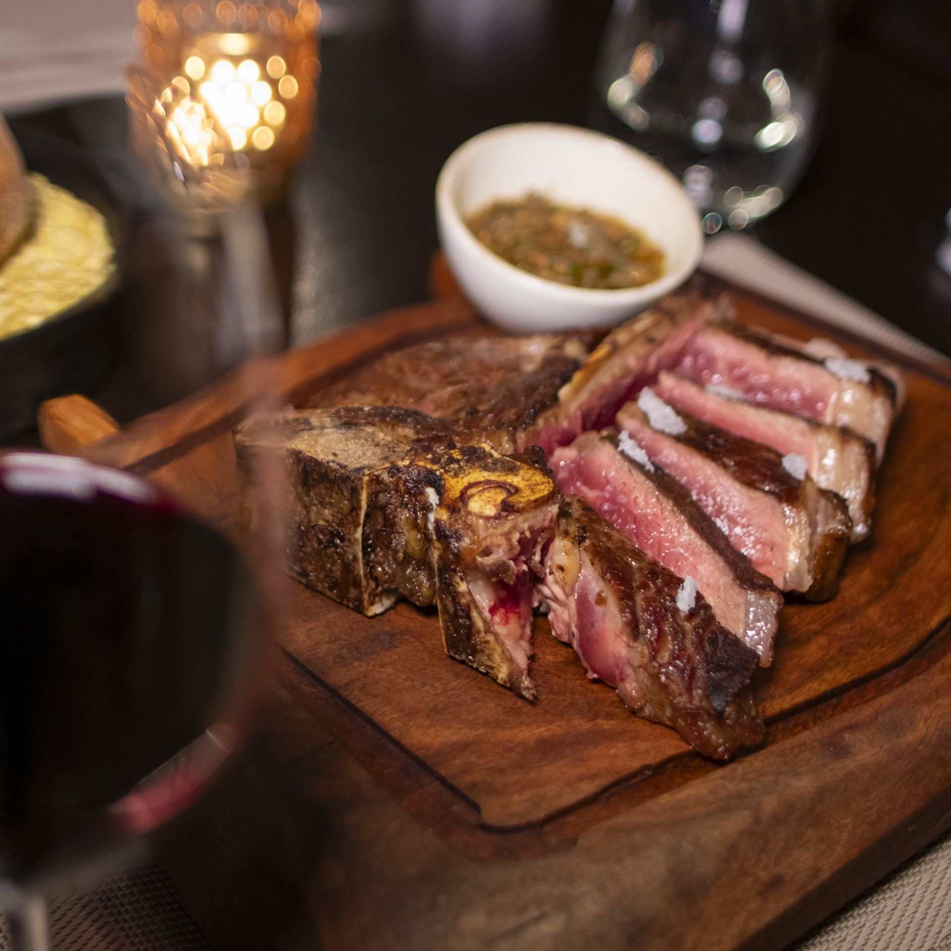 Un bistec sobre una tabla de cortar de madera junto a una copa de vino