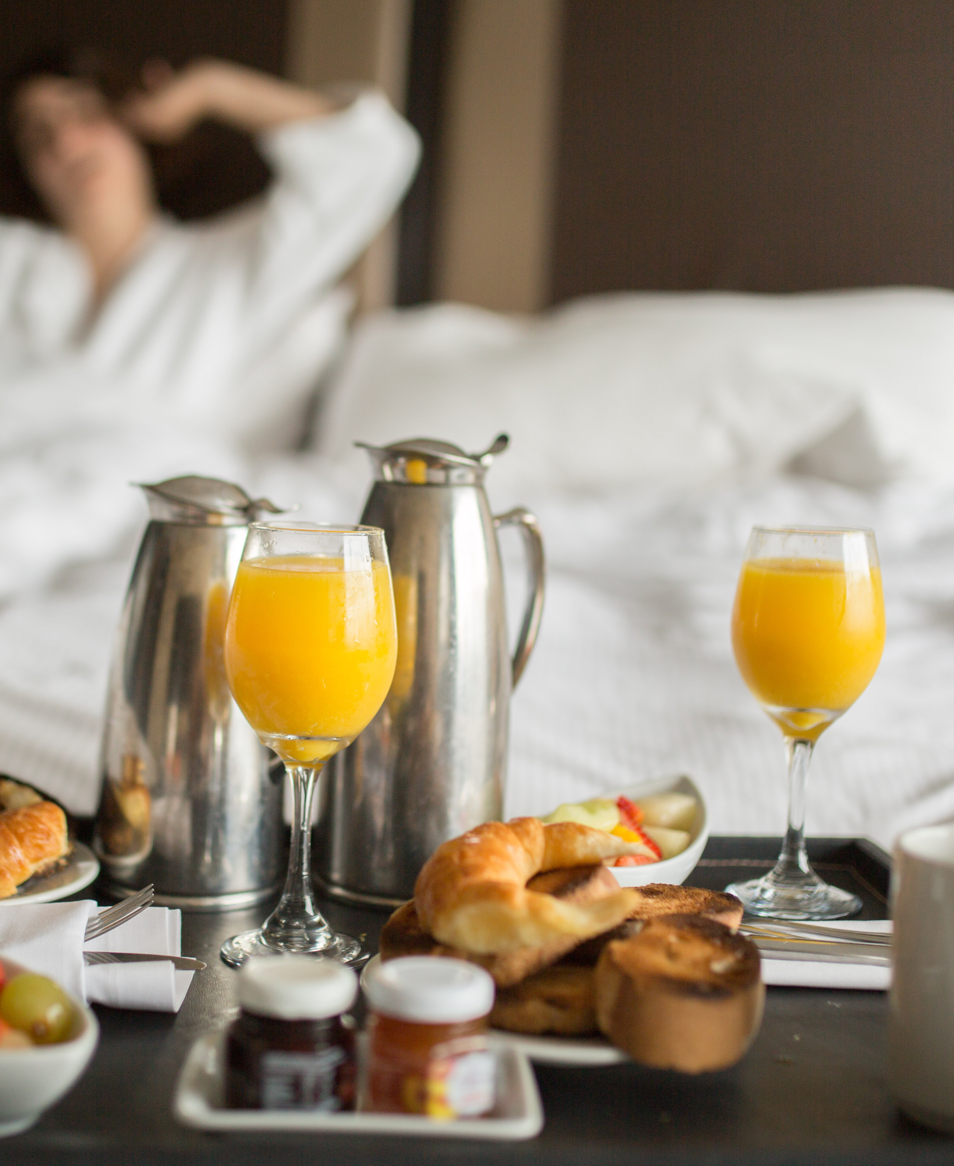 Una mujer está acostada en la cama con una bandeja de comida y bebidas.