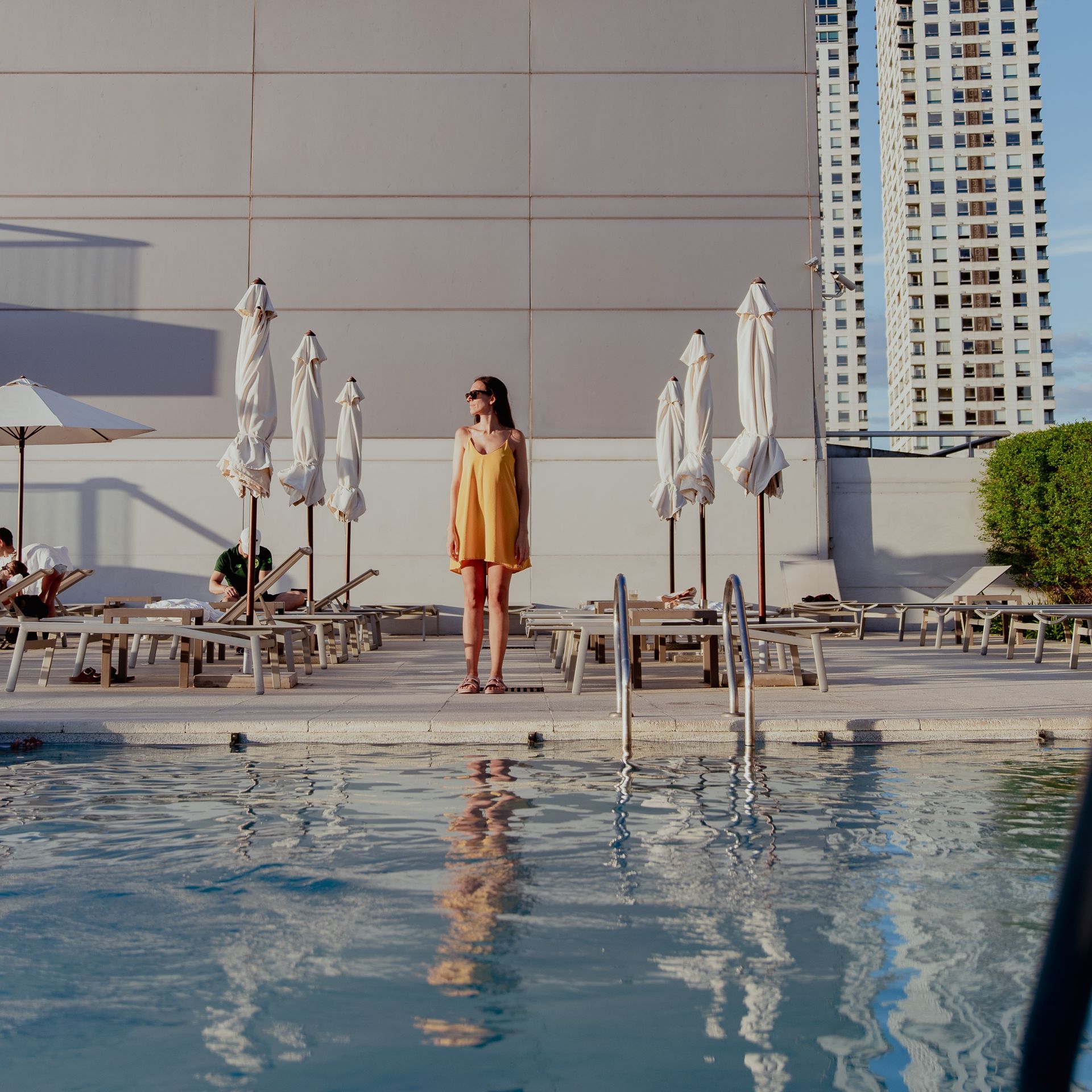Una mujer con un vestido amarillo está parada junto a una piscina.