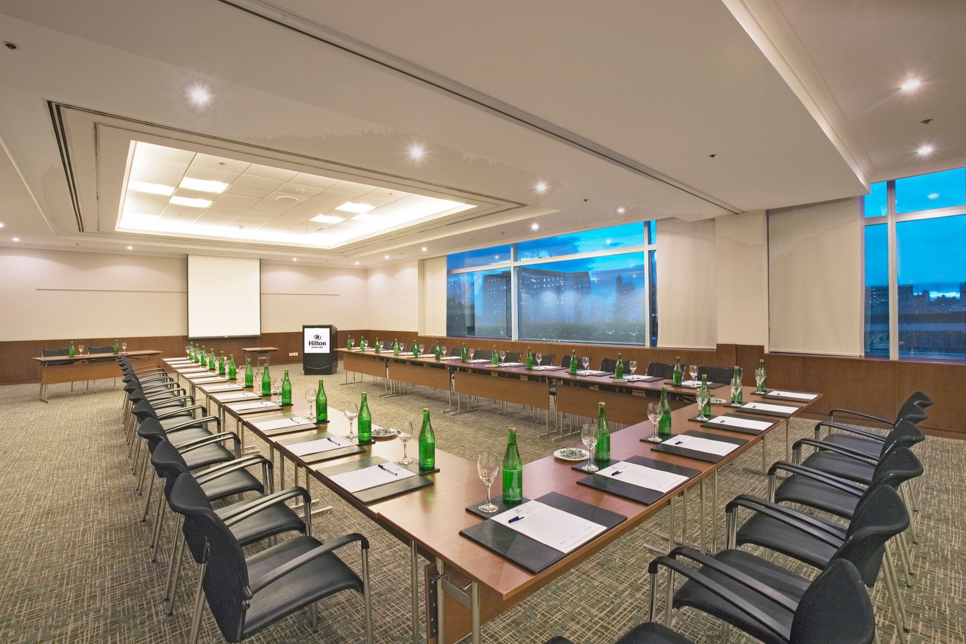 Una gran sala de conferencias con mesas y sillas preparadas para una reunión.