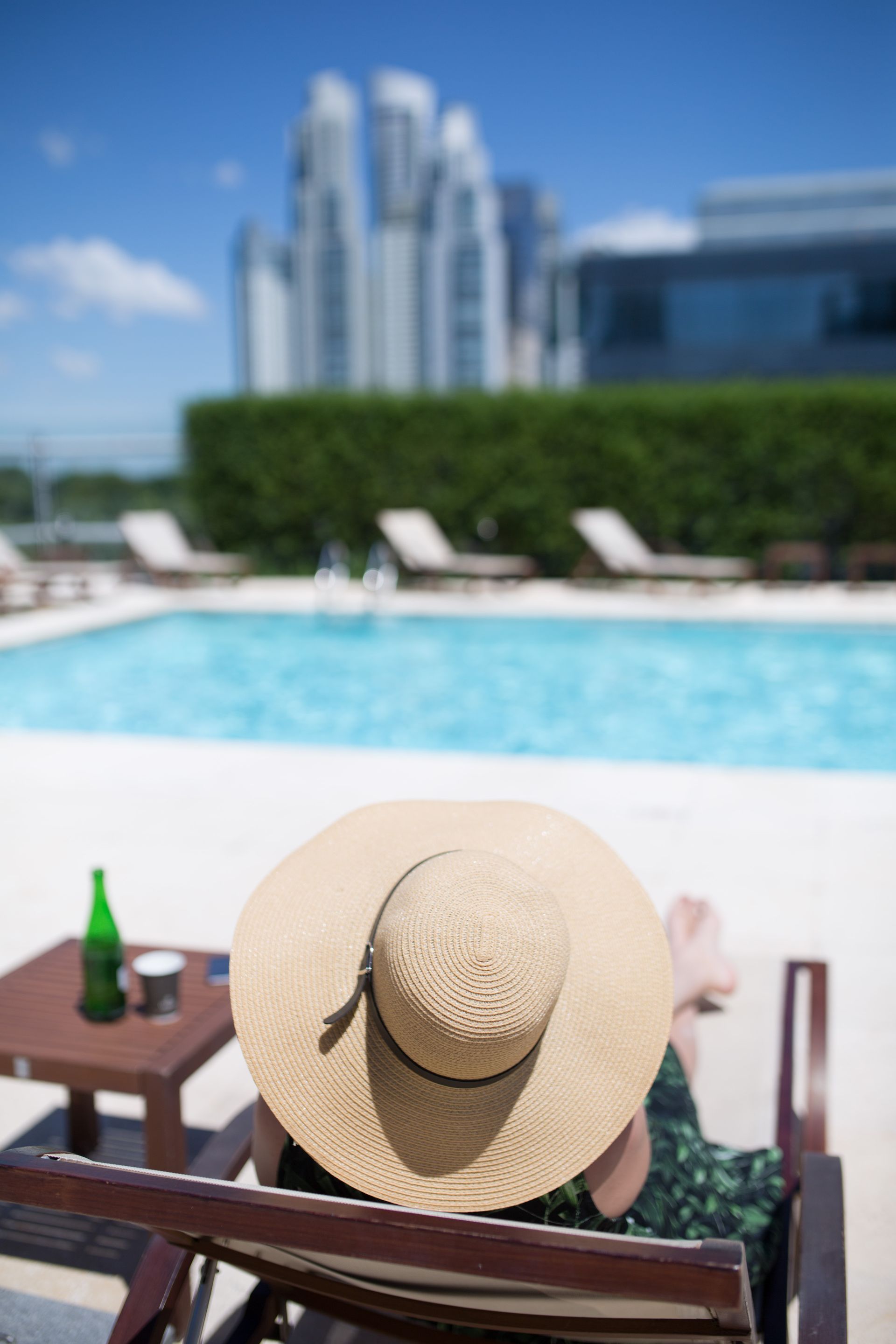 Una mujer con sombrero está sentada en una silla junto a una piscina.