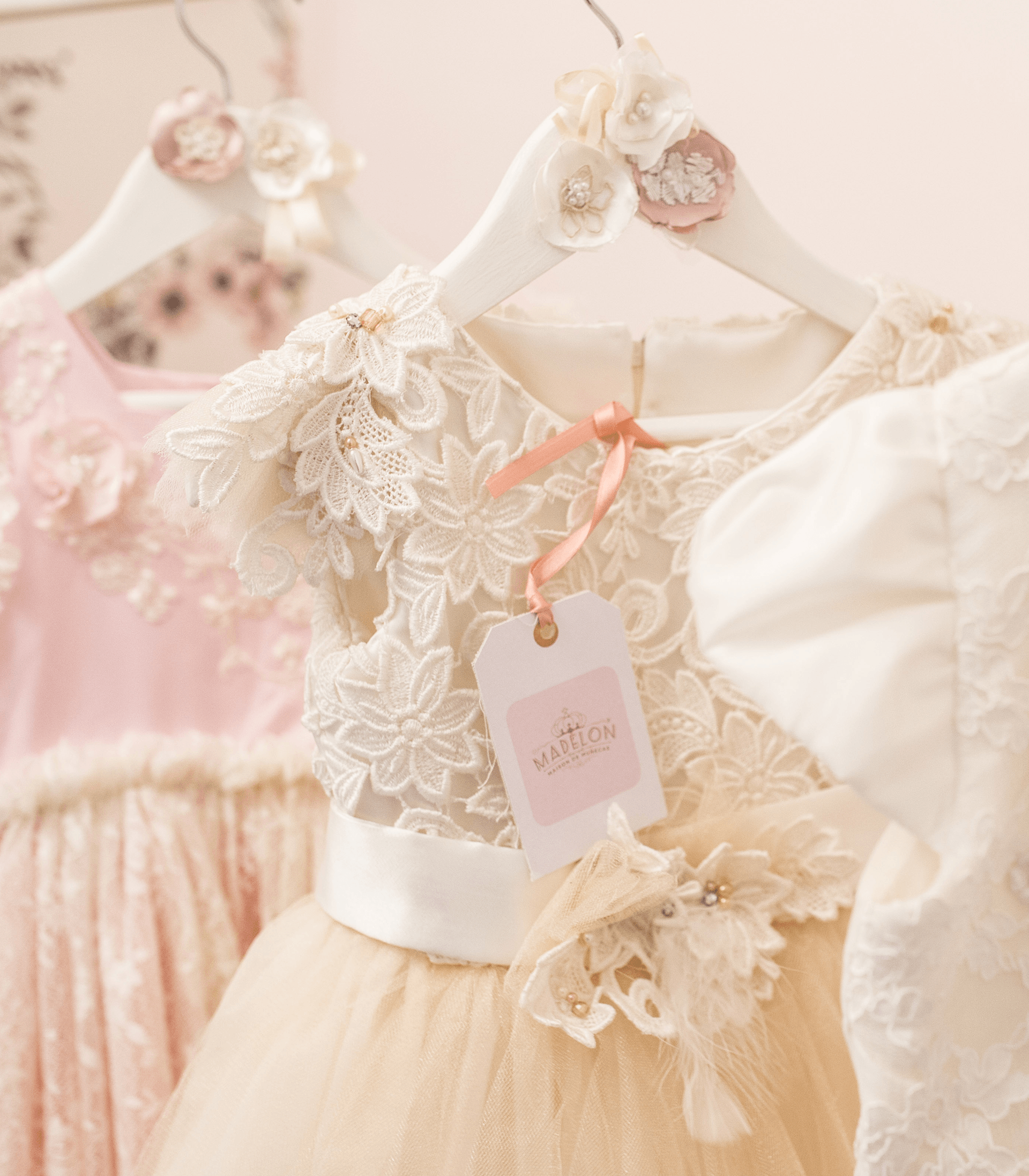Un vestido de encaje blanco cuelga de una percha blanca junto a un vestido rosa.
