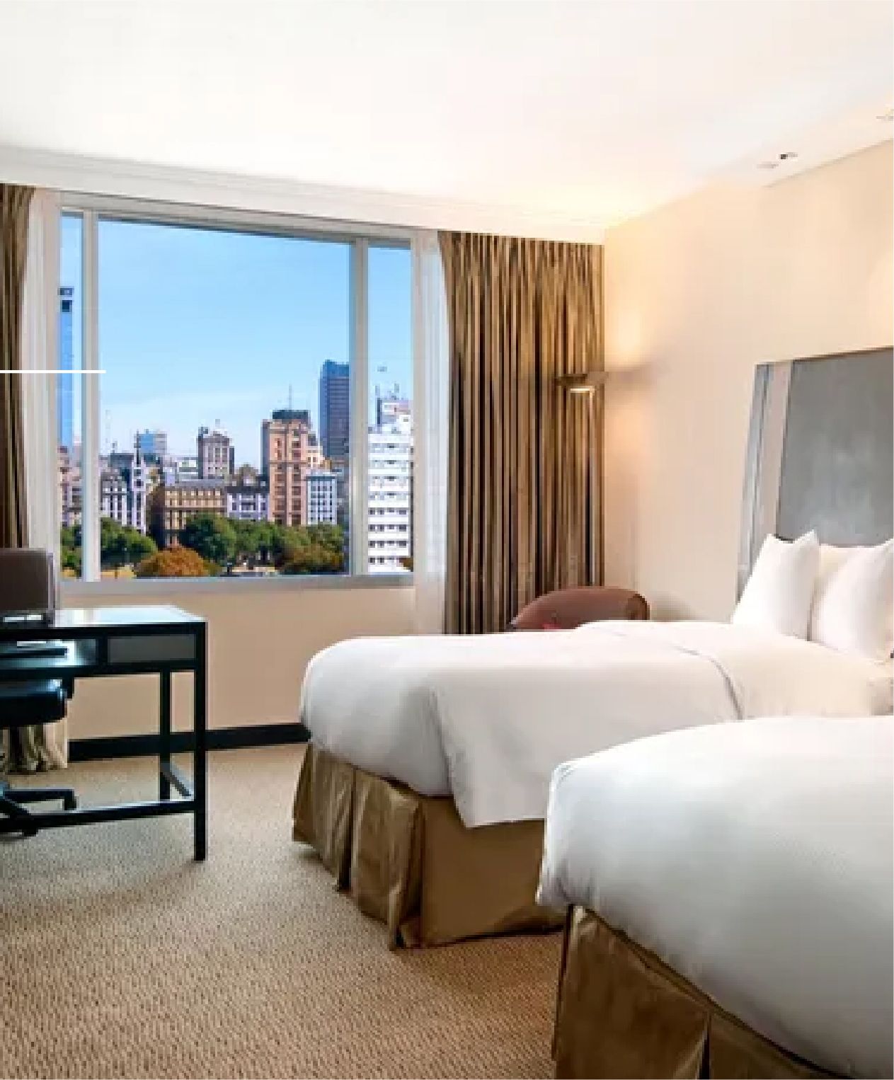 Una habitación de hotel con dos camas, un escritorio y un gran ventanal.