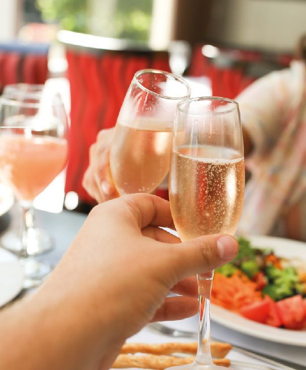 Una persona sostiene dos copas de champán frente a un plato de comida.