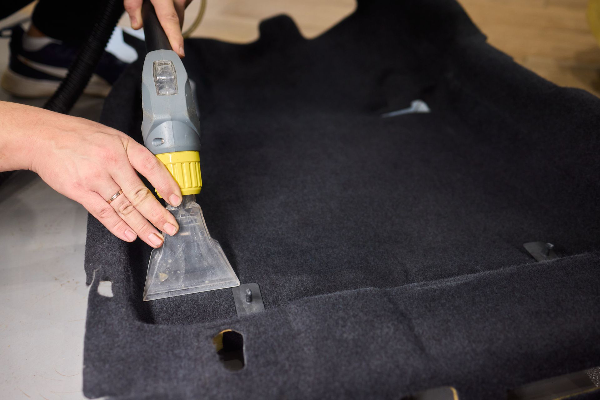 Person cleaning black car carpet with a handheld vacuum.