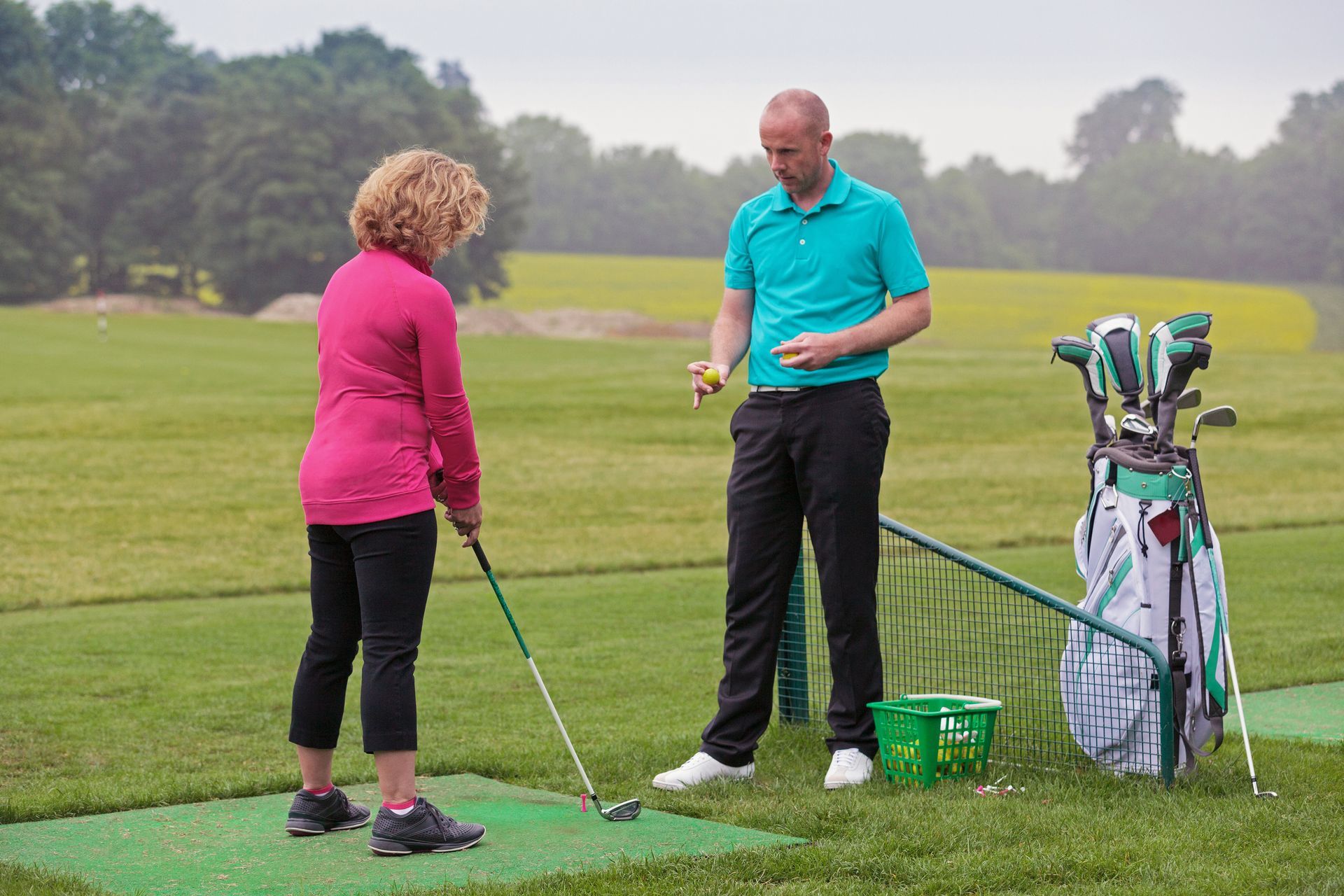 A man is teaching a woman how to play golf on a golf course.