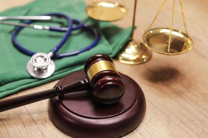 A judge 's gavel is sitting on a wooden table next to a stethoscope and scales.