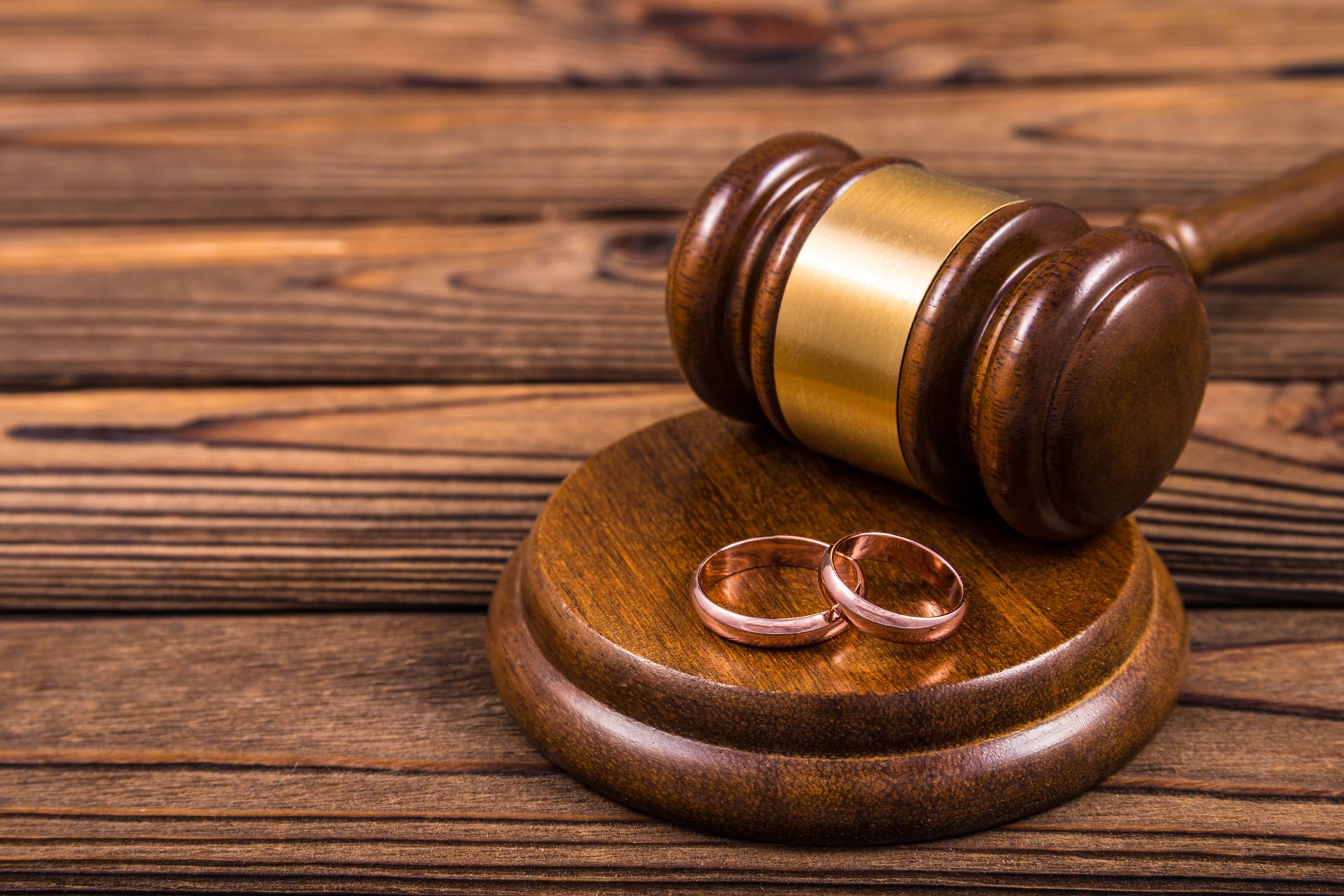 A pair of wedding rings sitting on top of a wooden gavel on a wooden table.