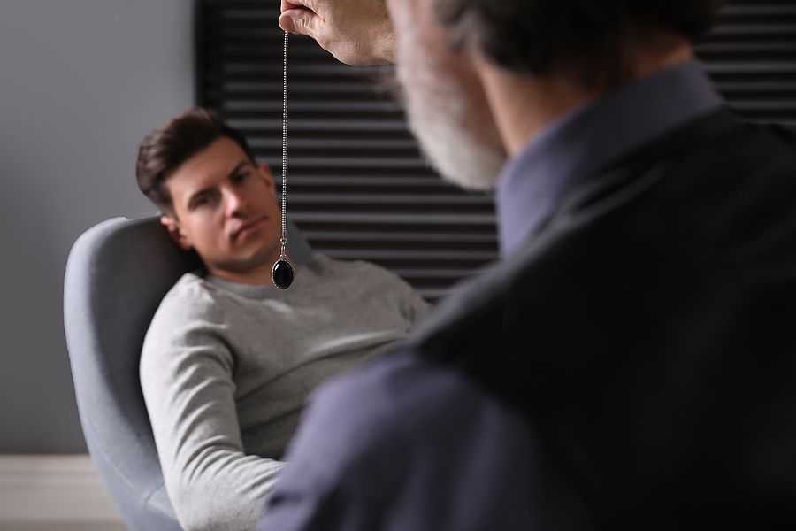 Man being hypnotized by a practitioner with a swinging pendant in a dimly lit room.