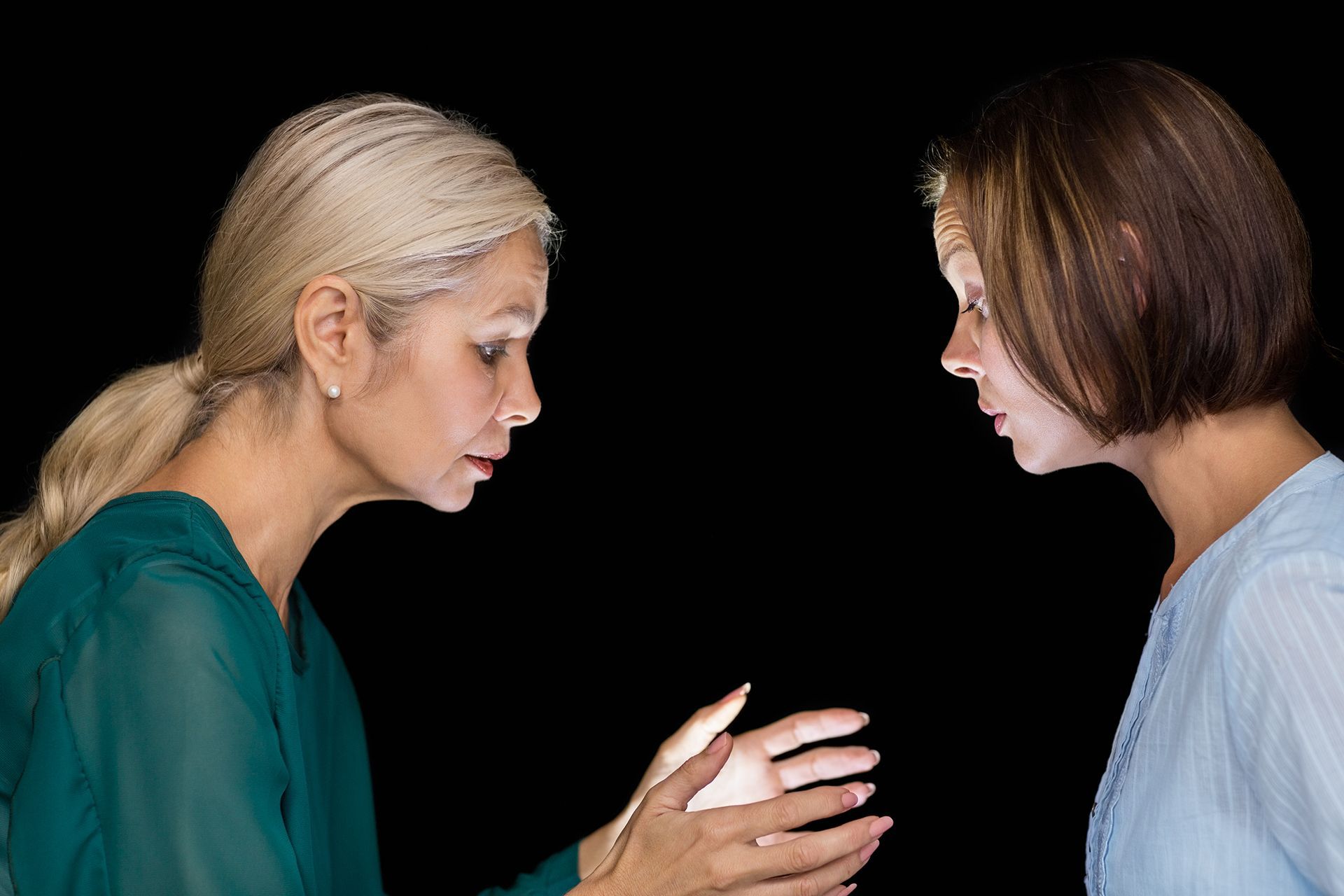 Woman in green dress holds glowing light, gazing at another woman.
