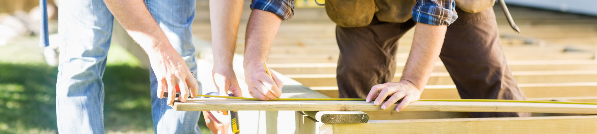 Two people measure and mark a wooden board on a construction site.