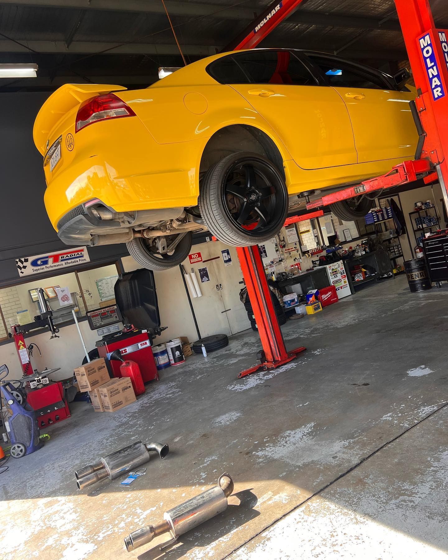 Yellow Car Raised High by a Lifter in a Garage — Certified Mechanic in Canberra, ACT