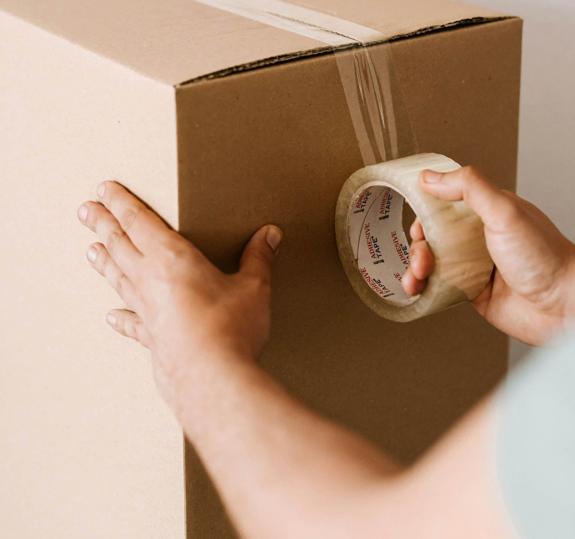 Person taping a cardboard box shut with clear tape.
