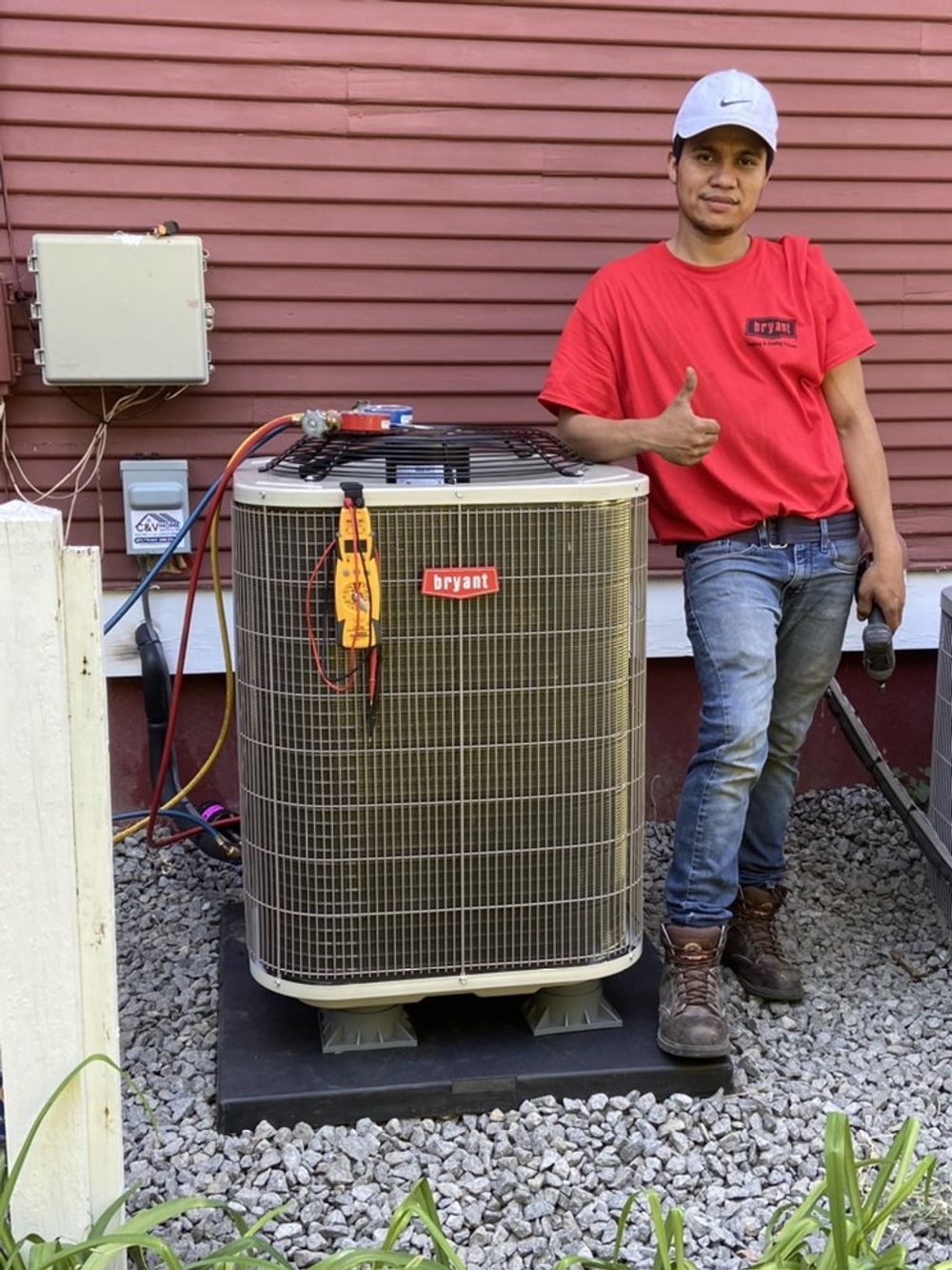 A technician uses a manifold gauge set to check refrigerant levels on an outdoor air conditioning unit.