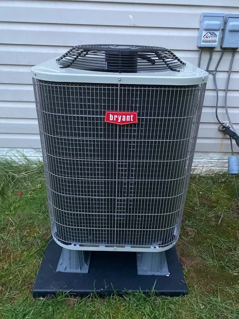 Hands wearing grey work gloves use a screwdriver to wire a ceiling fan component in a room with large windows.