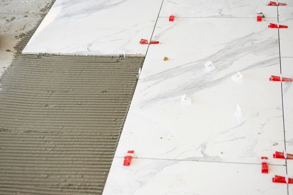 Marble floor tiles being installed over gray adhesive with red spacers along the seams