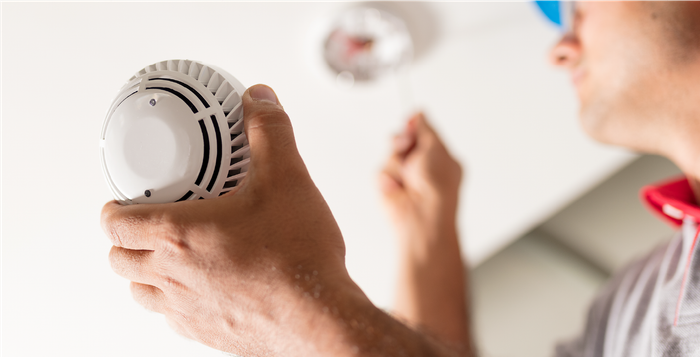 A man is holding a smoke detector in his hands.