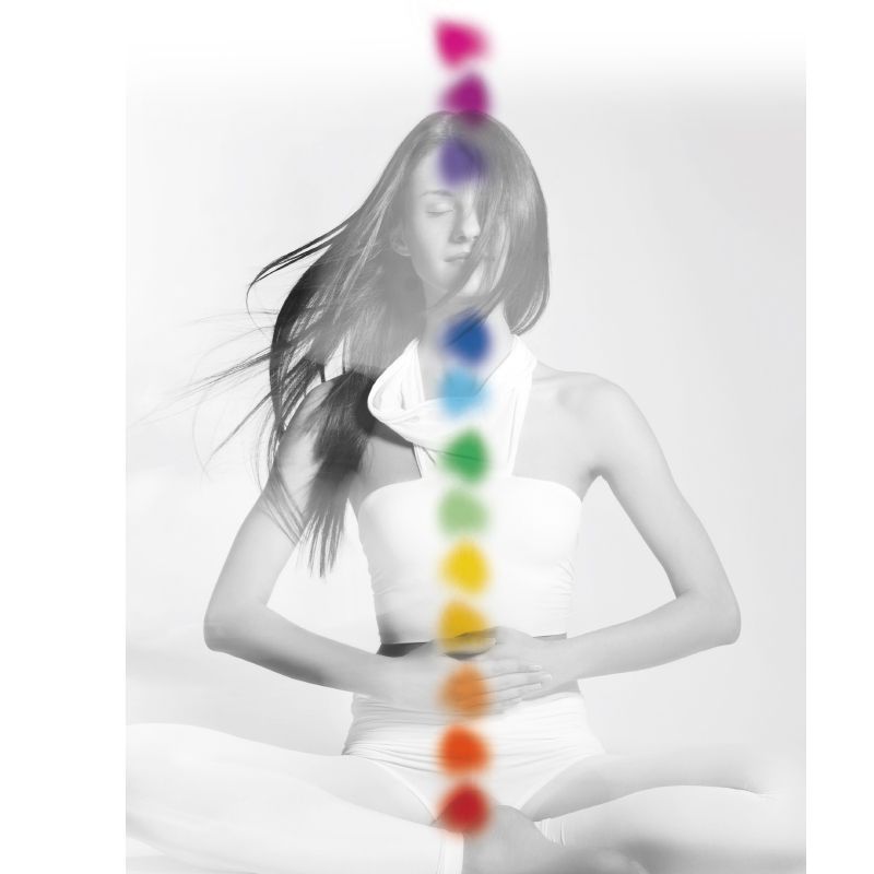 Eine Frau sitzt im Lotussitz und ist von einem Regenbogen aus Chakren umgeben