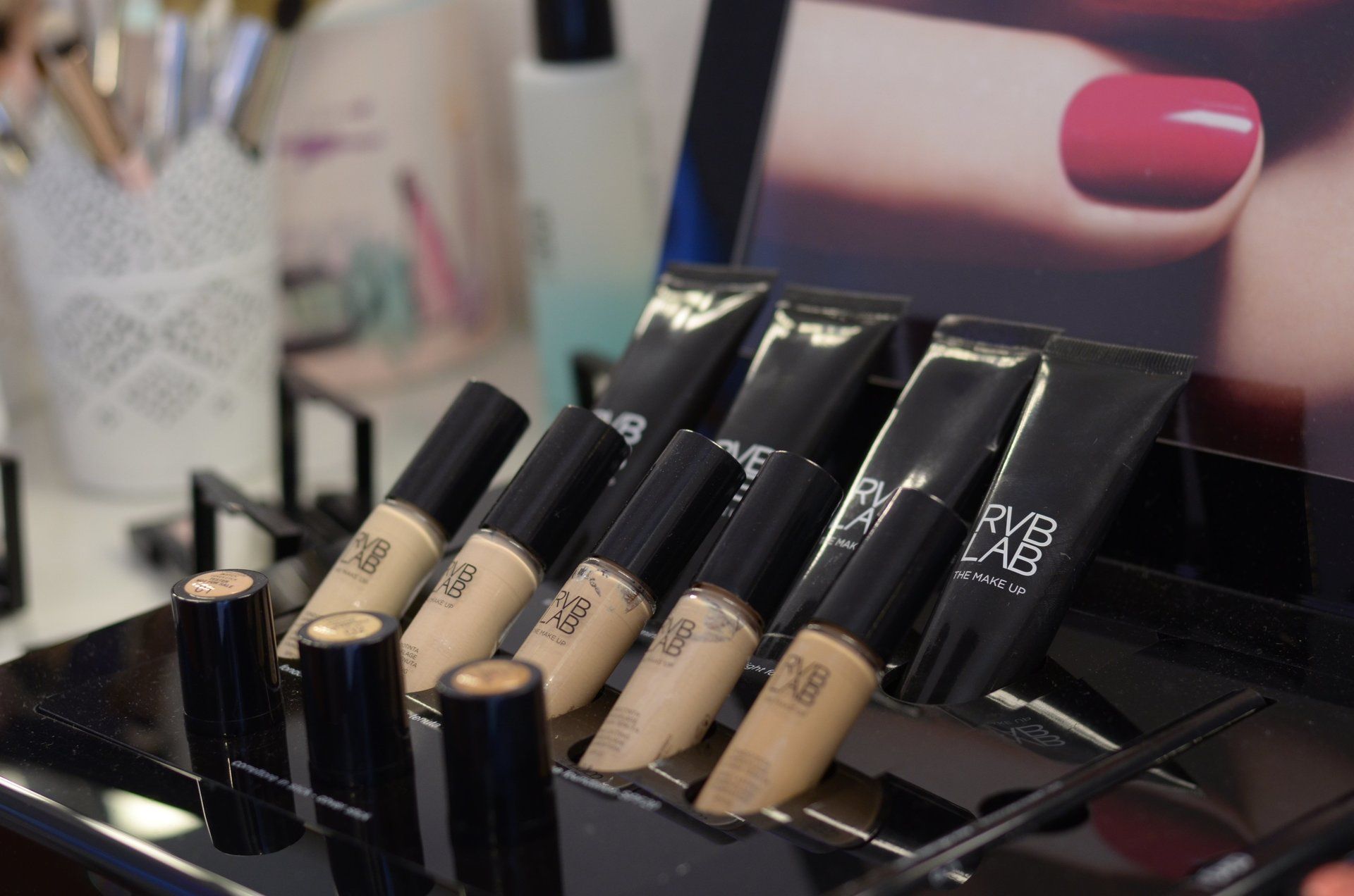 Eine Anzeige von Concealer-Tuben mit einem Bild einer Frauenhand im Hintergrund