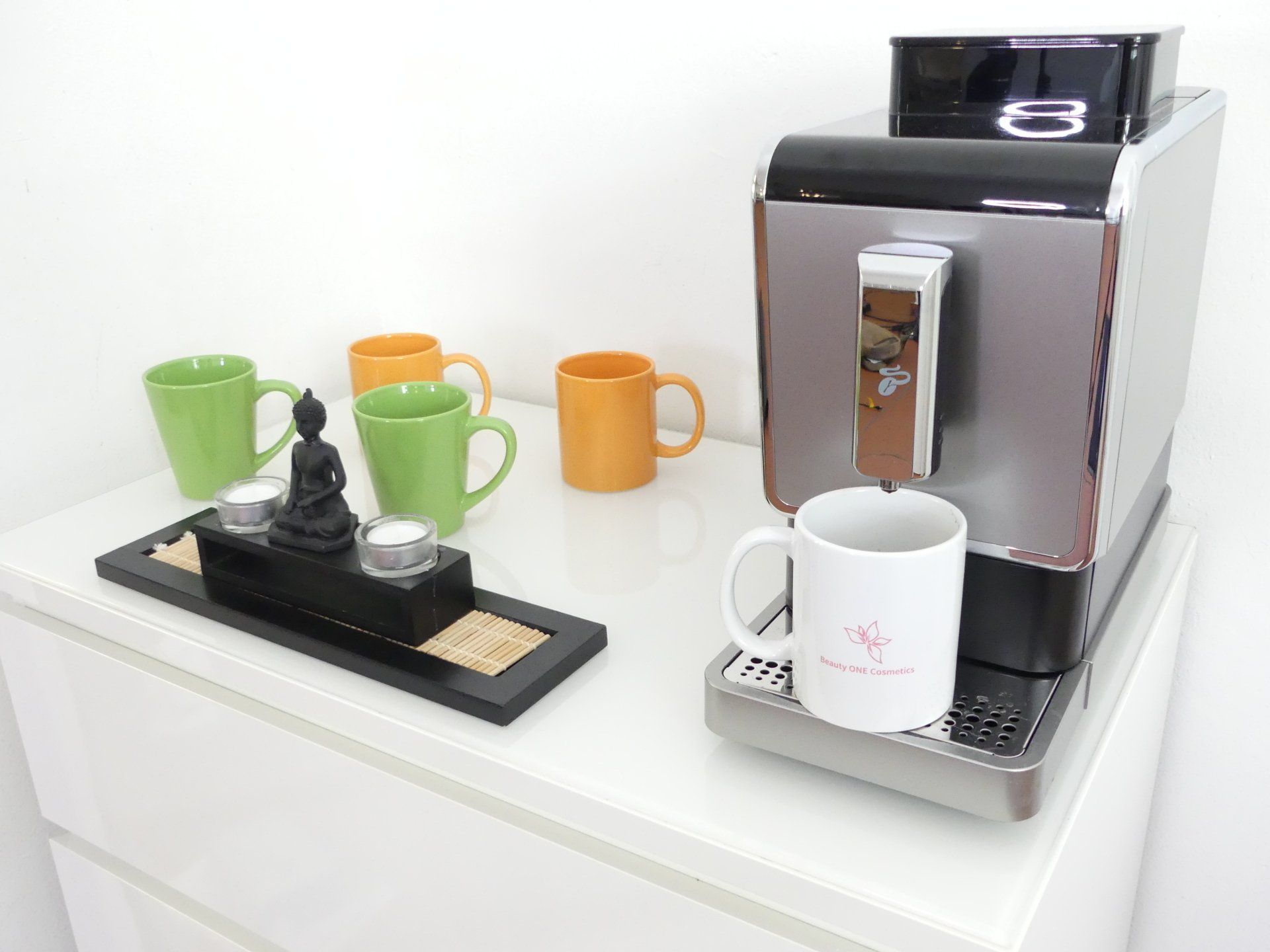 Auf einem Tisch steht eine Kaffeemaschine neben einem Tablett mit Tassen und Kerzen.