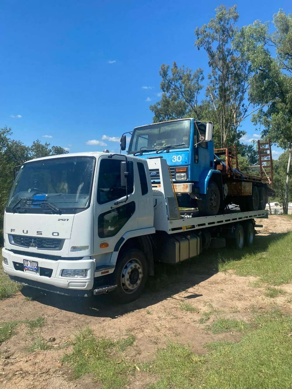 A White Tow Truck With a Blue Truck on the Back is Parked on a Dirt Road — ASAP Towing Pty Ltd in Urangan, QLD