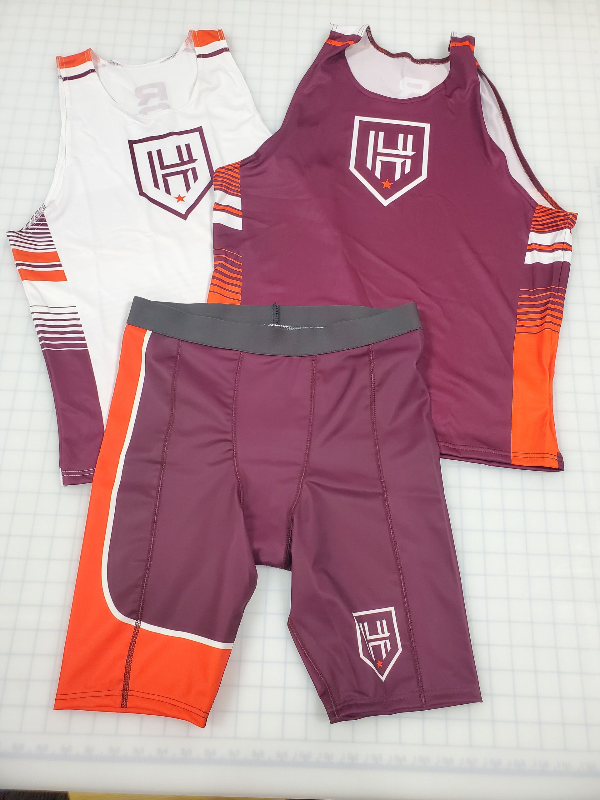 Two athletic jerseys and athletic shorts, white/purple/orange and maroon/orange, with a logo on each garment.