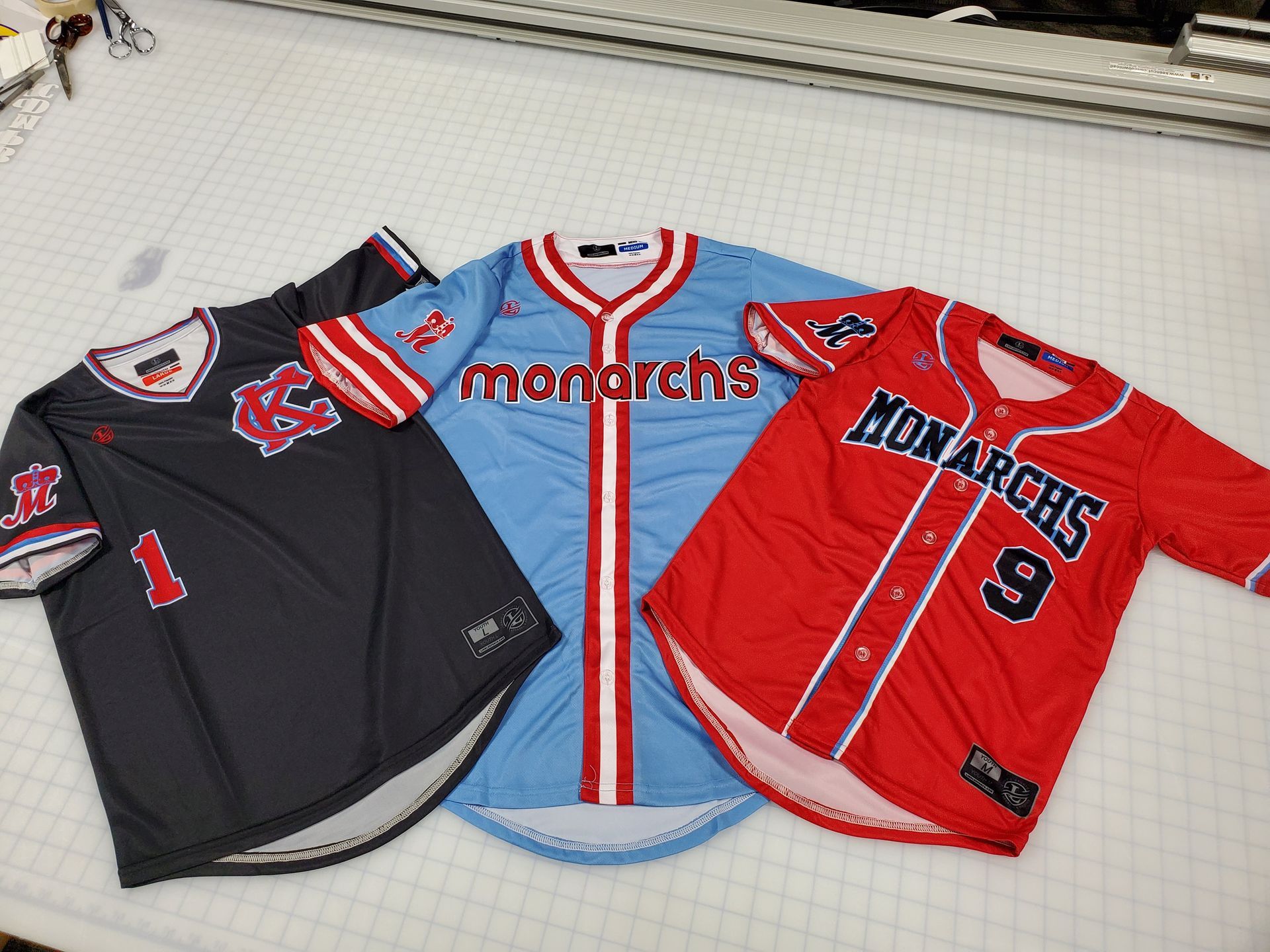 Three baseball jerseys: black, blue, and red