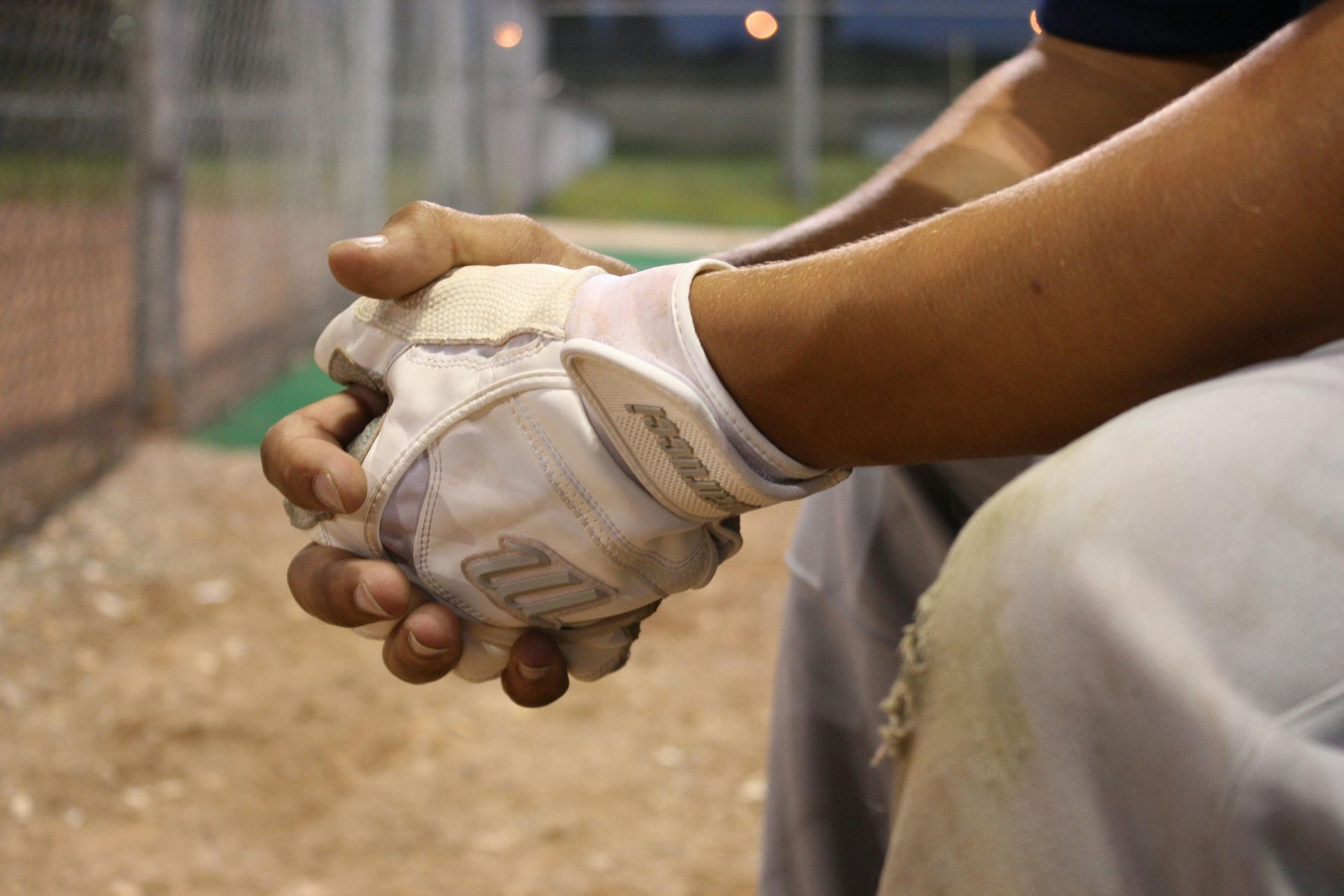 Baseball player's hands clasped, wearing a glove and seated near a baseball field.