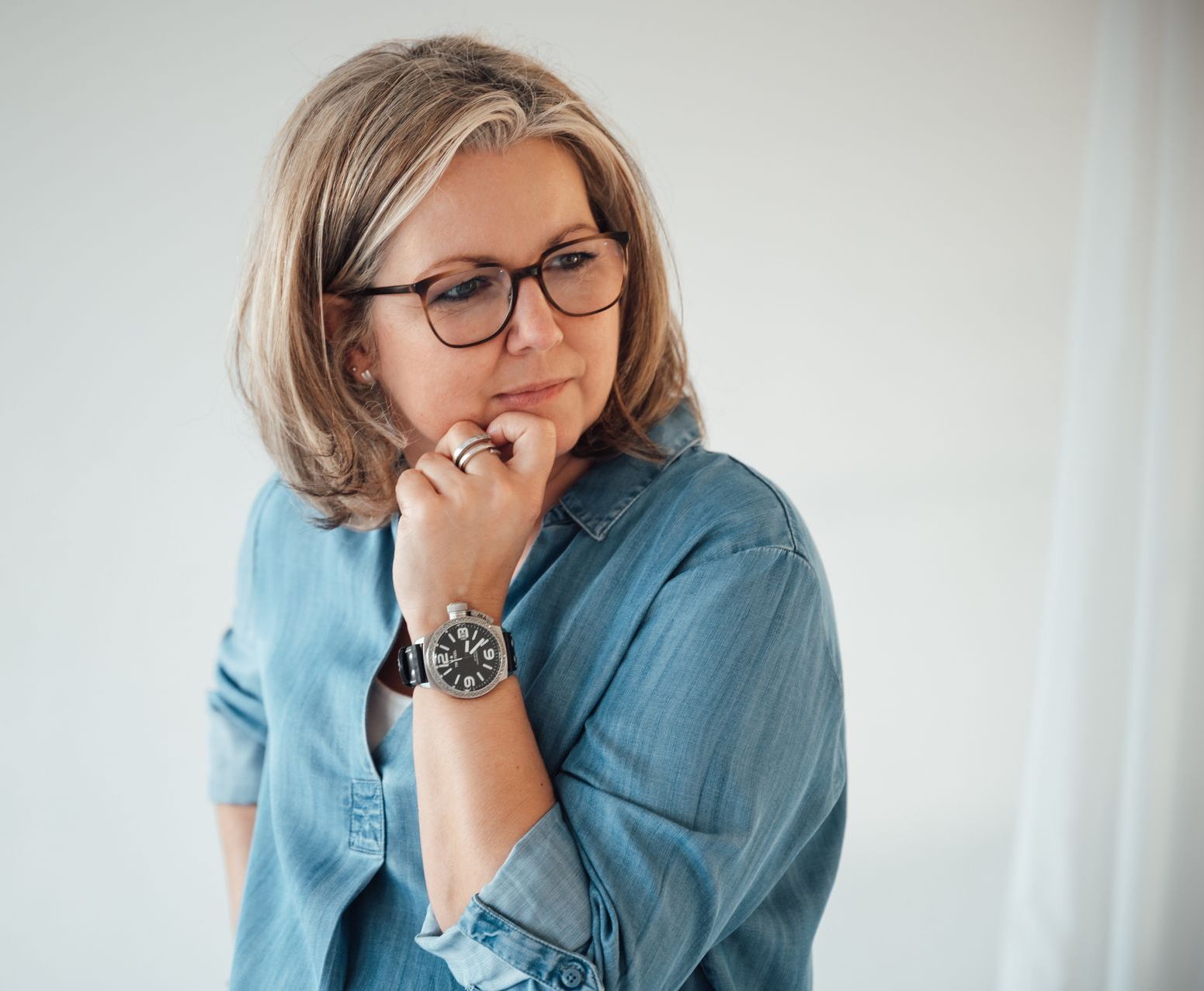 Eine Frau (ich) in blauer  Bluse, steht Gedankenversunkenen vor einem weißen Hintergrund.