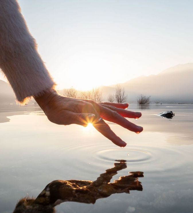 Frau hält Hand über Wasserspiegel und fängt Sonnenlicht ein