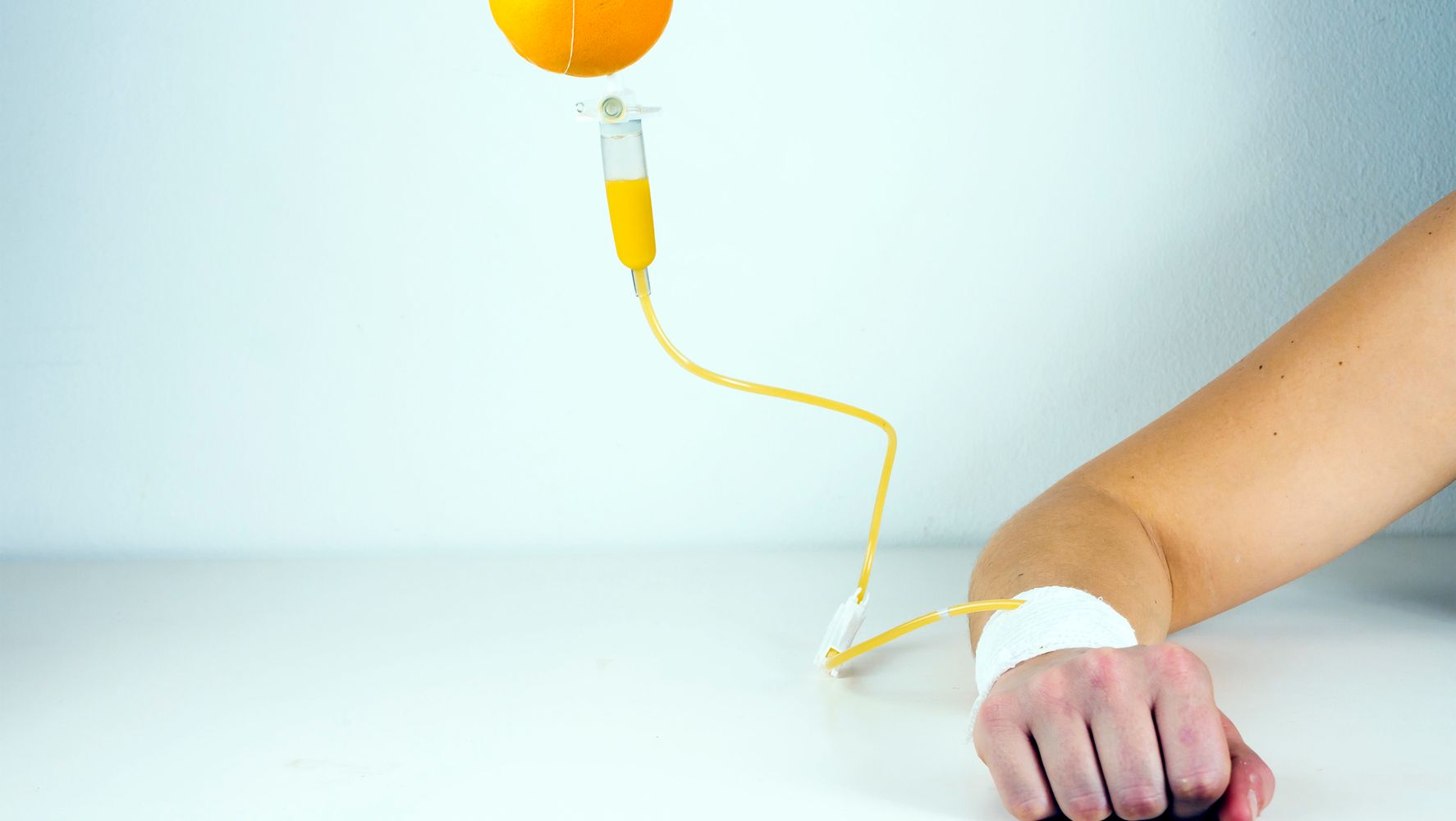 Orange juice in an IV set-up going into gauze on a person's arm
