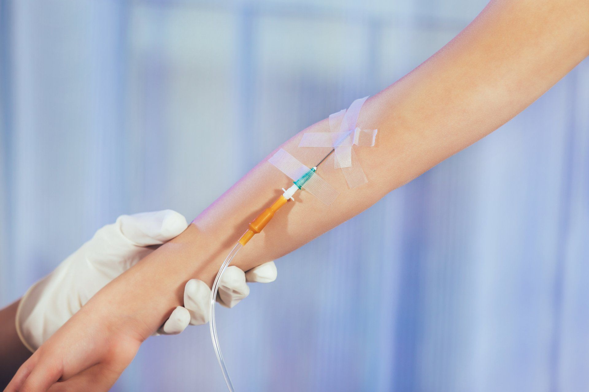 IV needle going into a person's arm with a gloved hand holding the arm