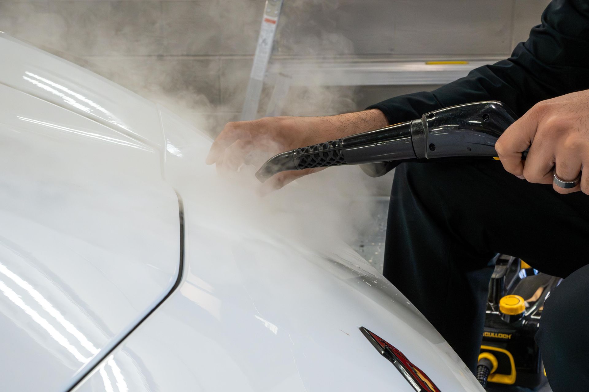 Person steaming a white car hood. Steam is visible.