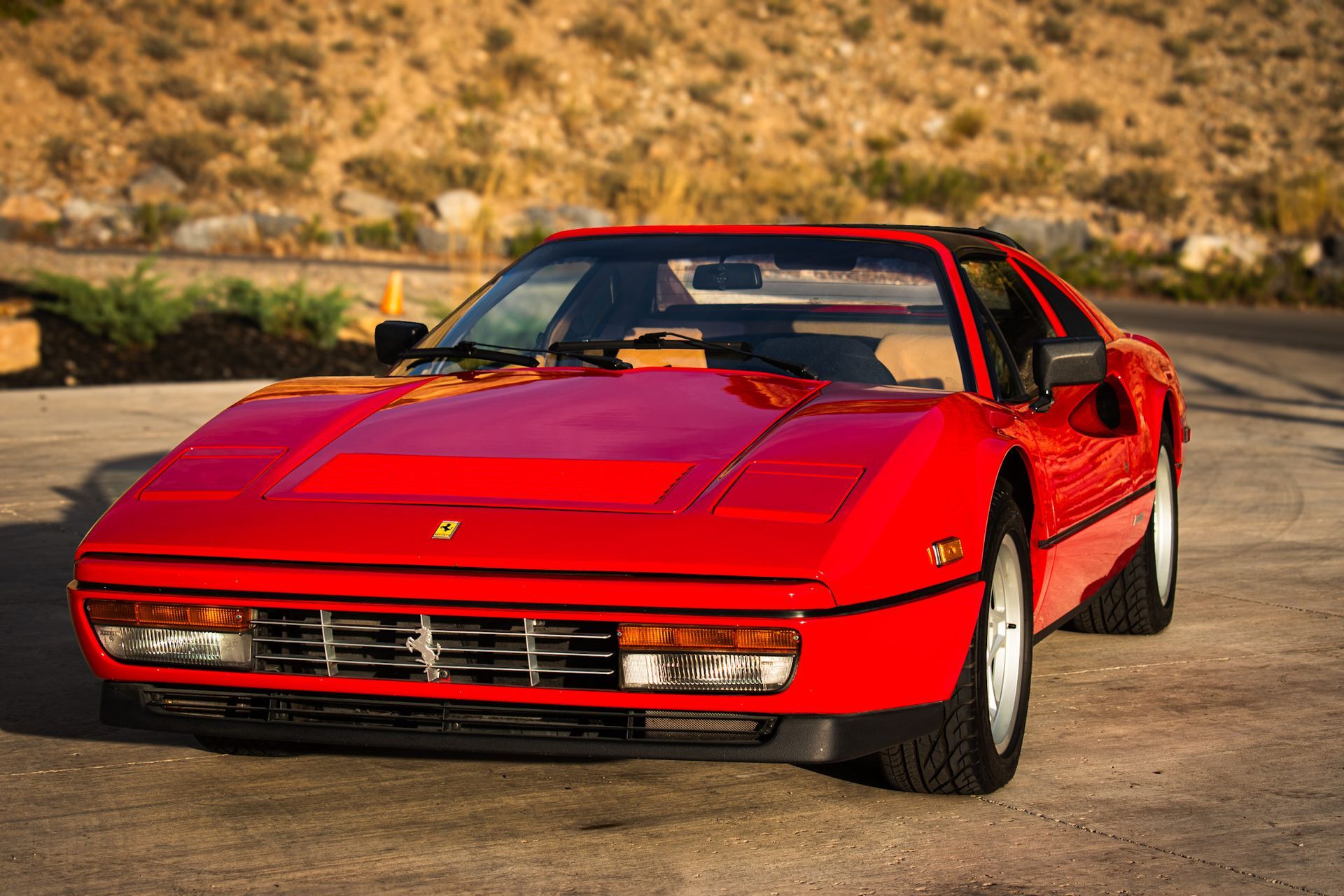 Red Ferrari sports car parked on a road, with a beige interior and a desert backdrop.
