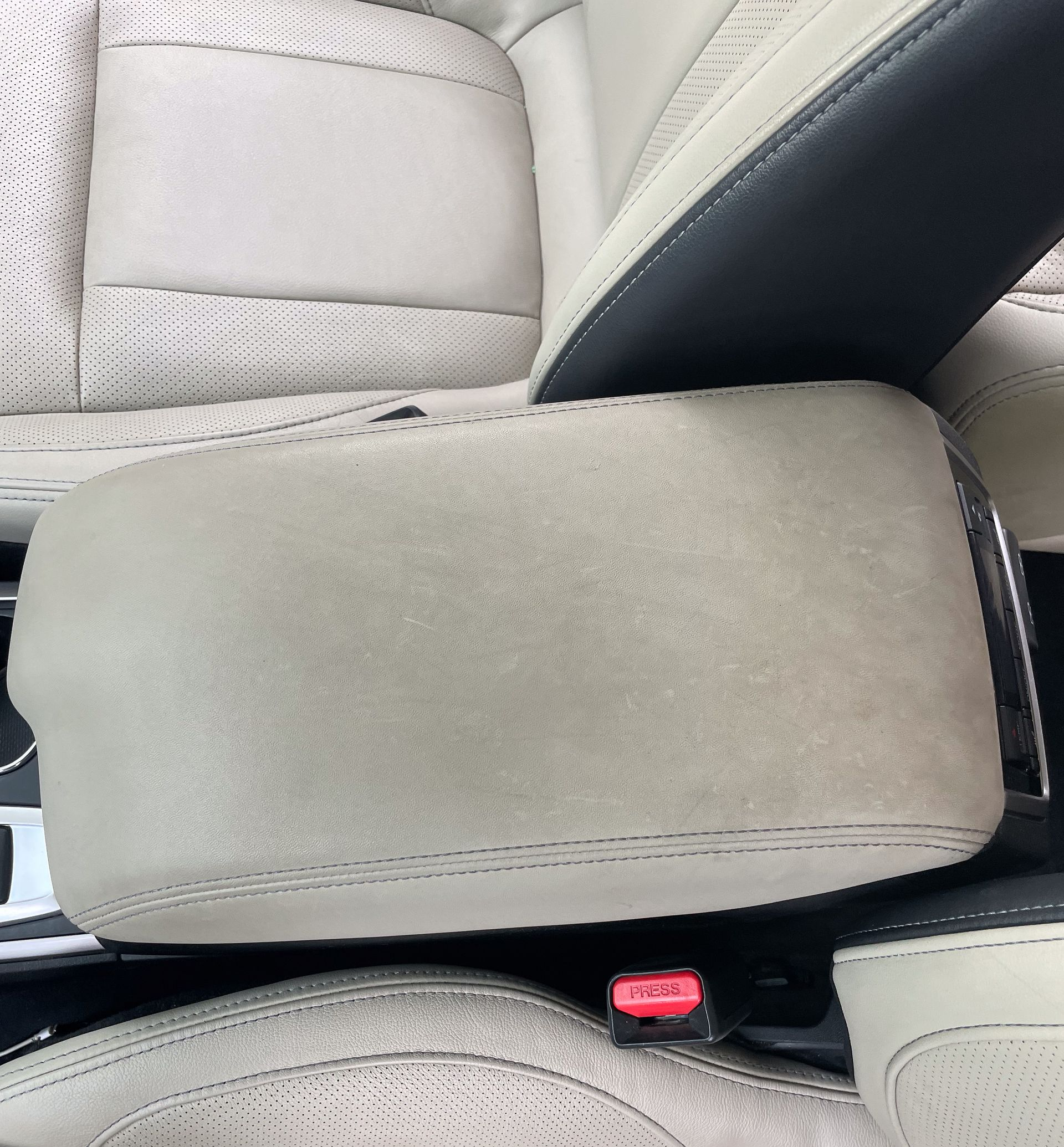 Beige car armrest with stitching, against light-colored patterned seats.