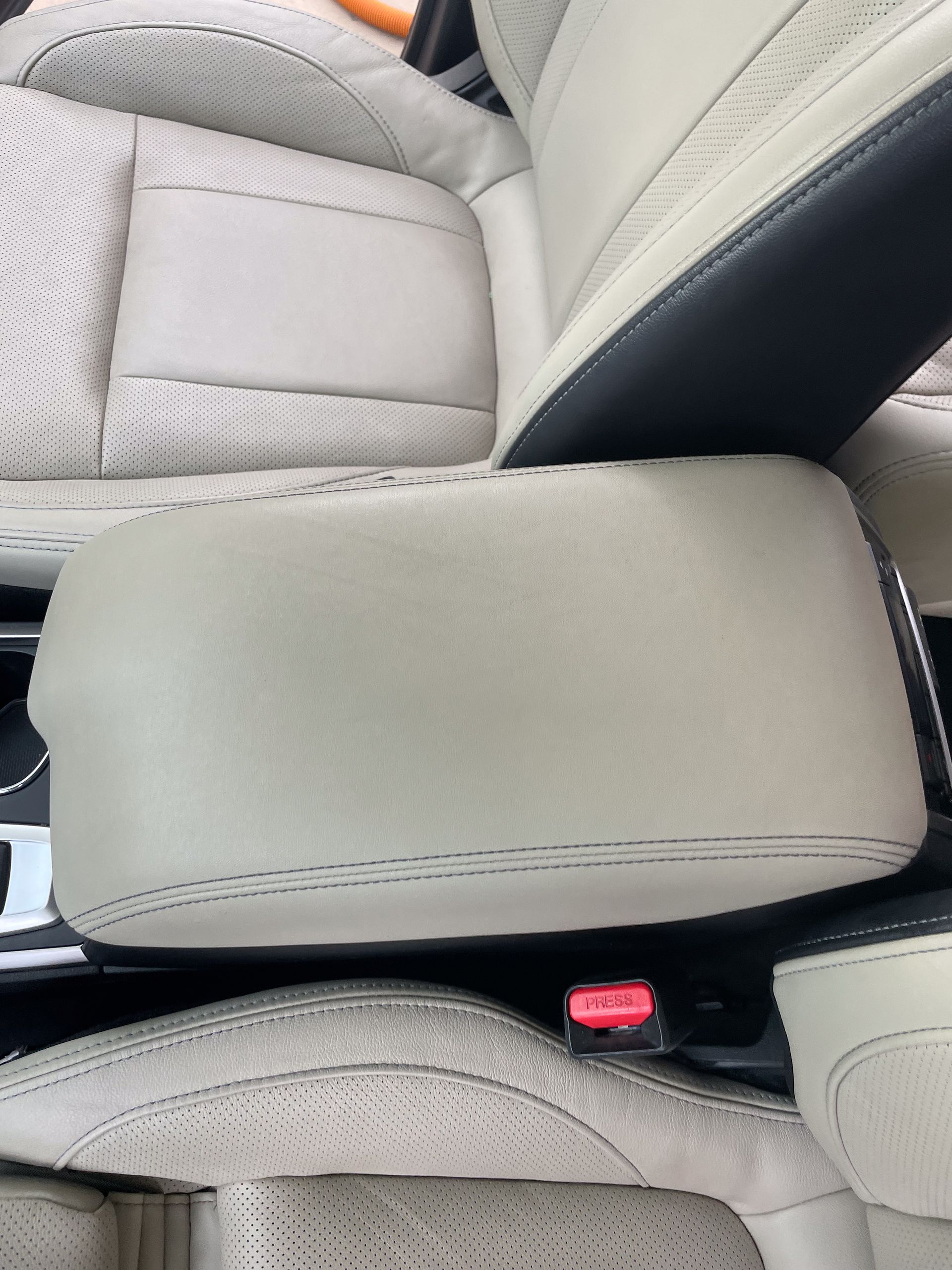 Beige car interior with center console, armrest, and seat belt buckle visible.
