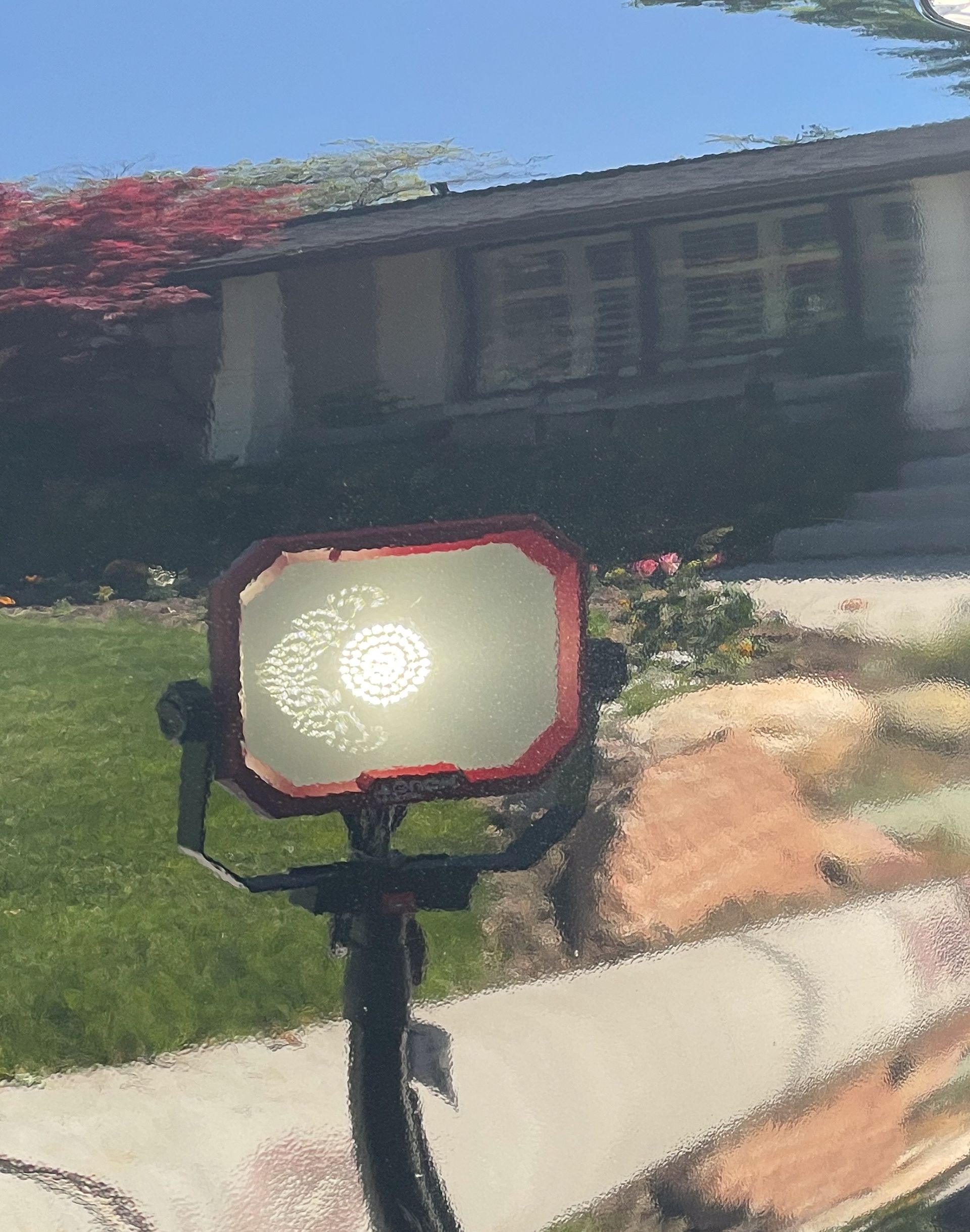 Red work light on tripod in front of a house.