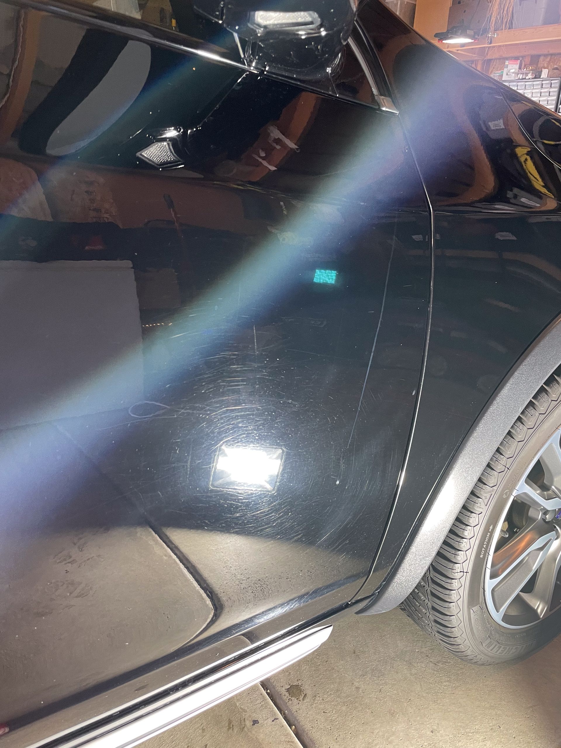 Black car door with scratches, near a tire and a step bar, with a light flare.